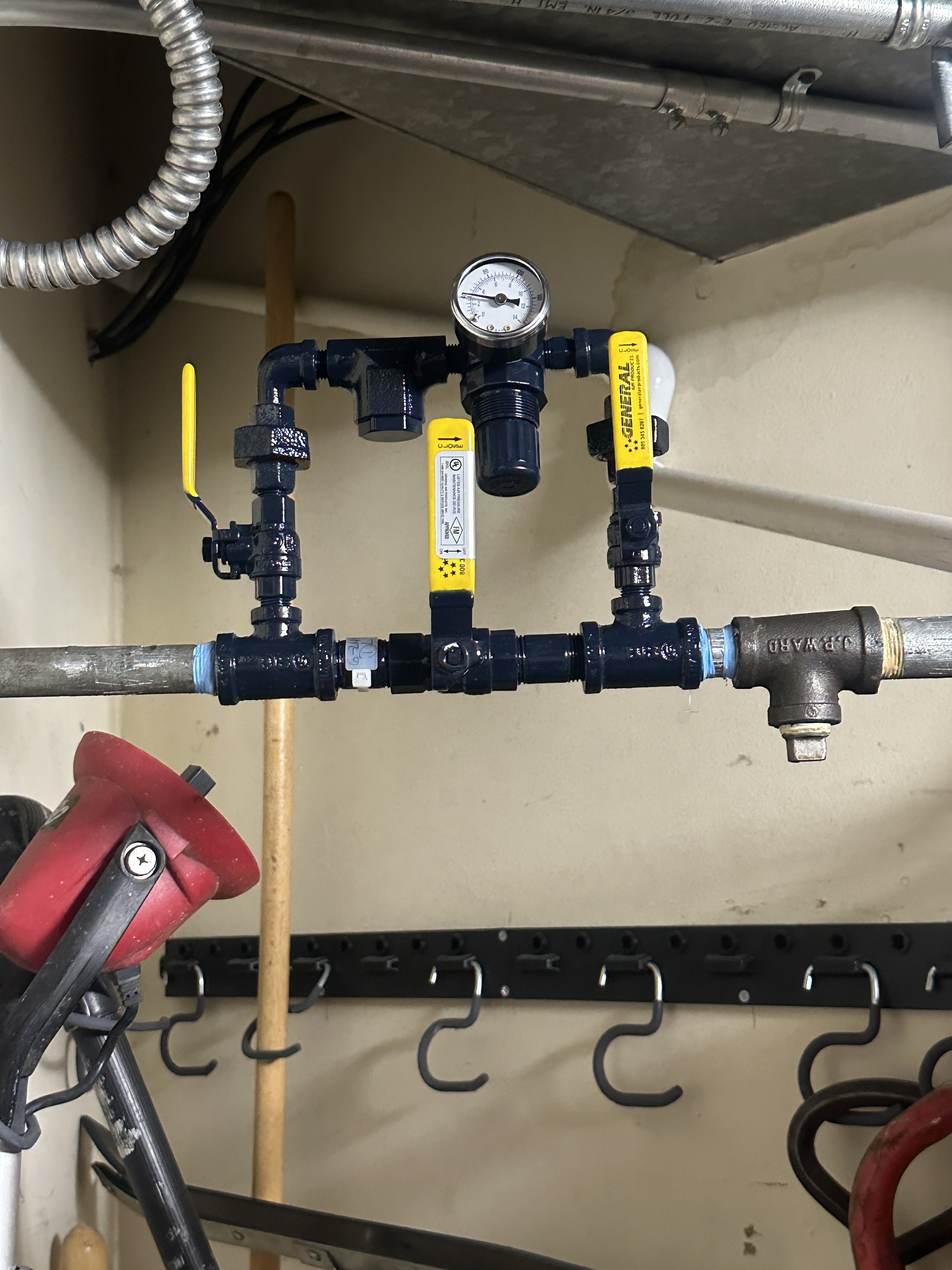 Close-up of plumbing pipes and a pressure gauge inside a utility closet or work area.