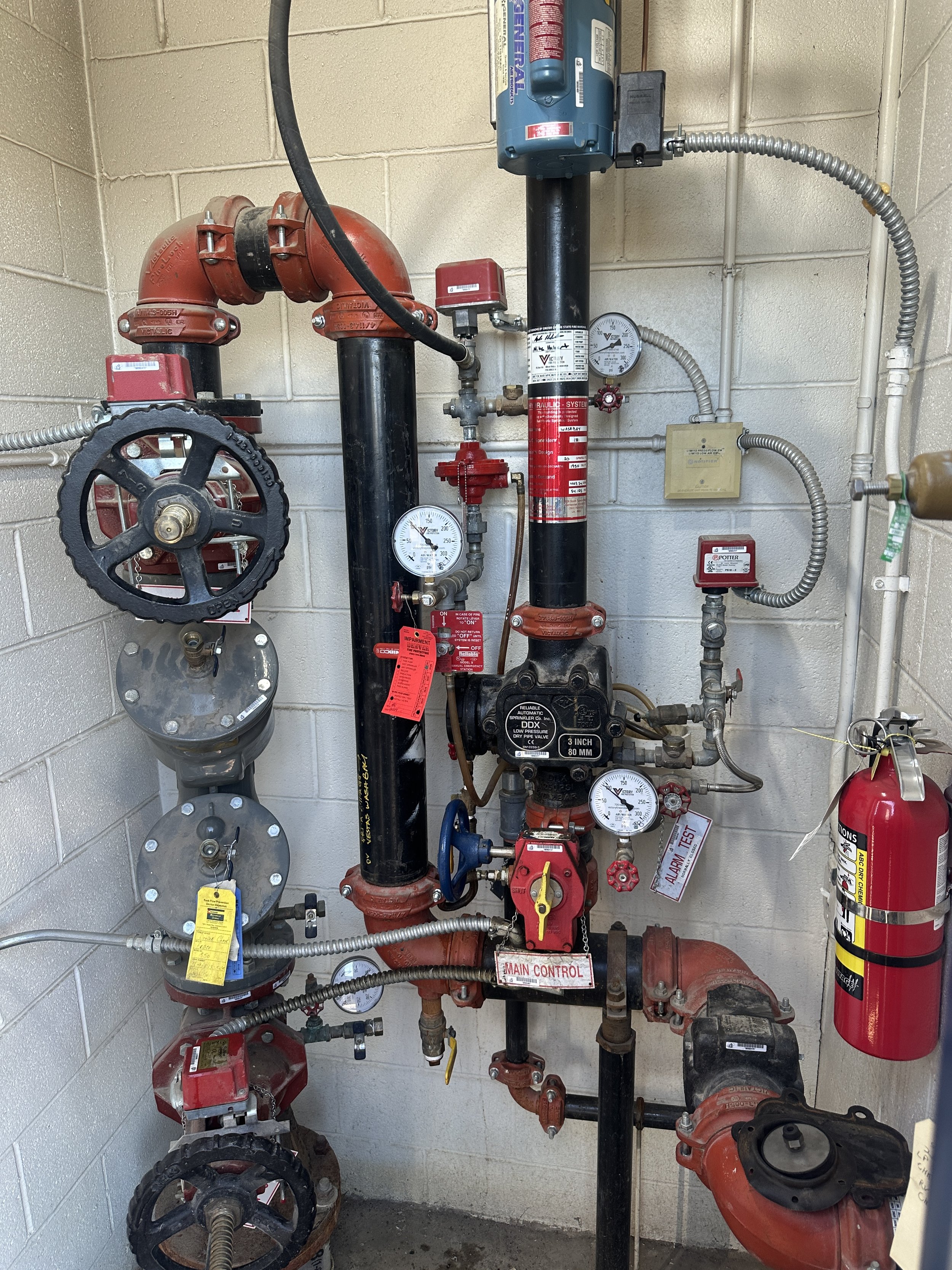 Fire suppression system with various piping, gauges, valves, and a fire extinguisher mounted on a wall.