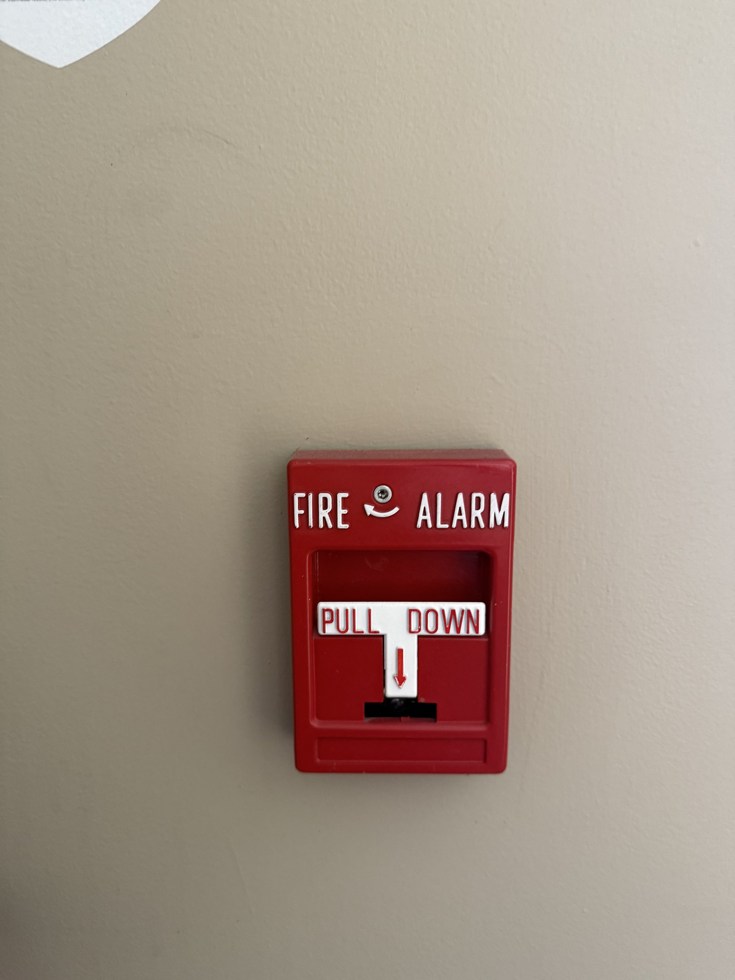 Red fire alarm pull station on a beige wall with white lettering.
