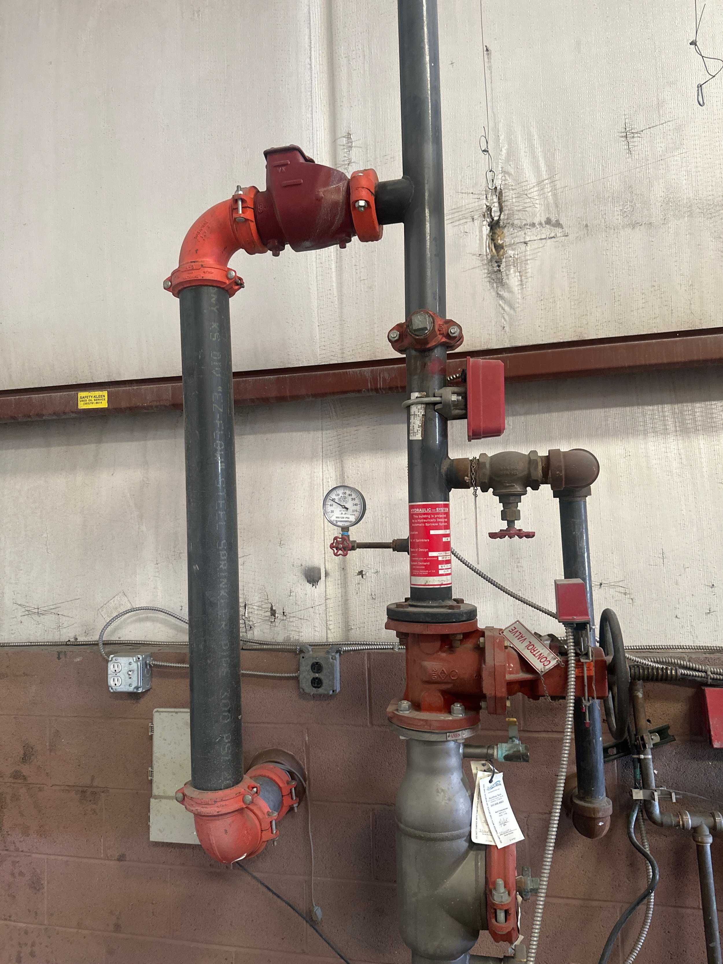 A fire sprinkler system with pipes, valves, and a pressure gauge mounted on a wall in a building