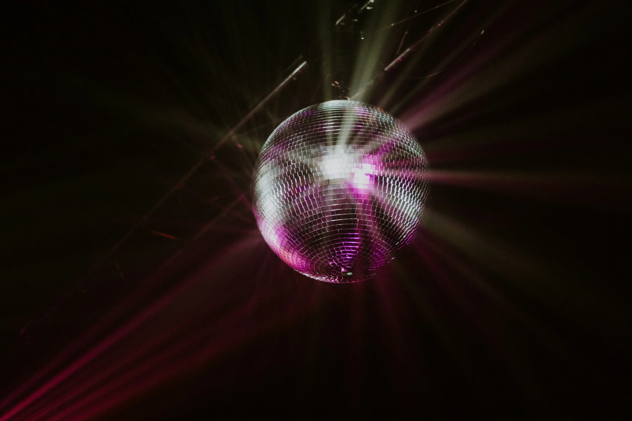 A disco ball reflecting pink and purple lights in a dark room.