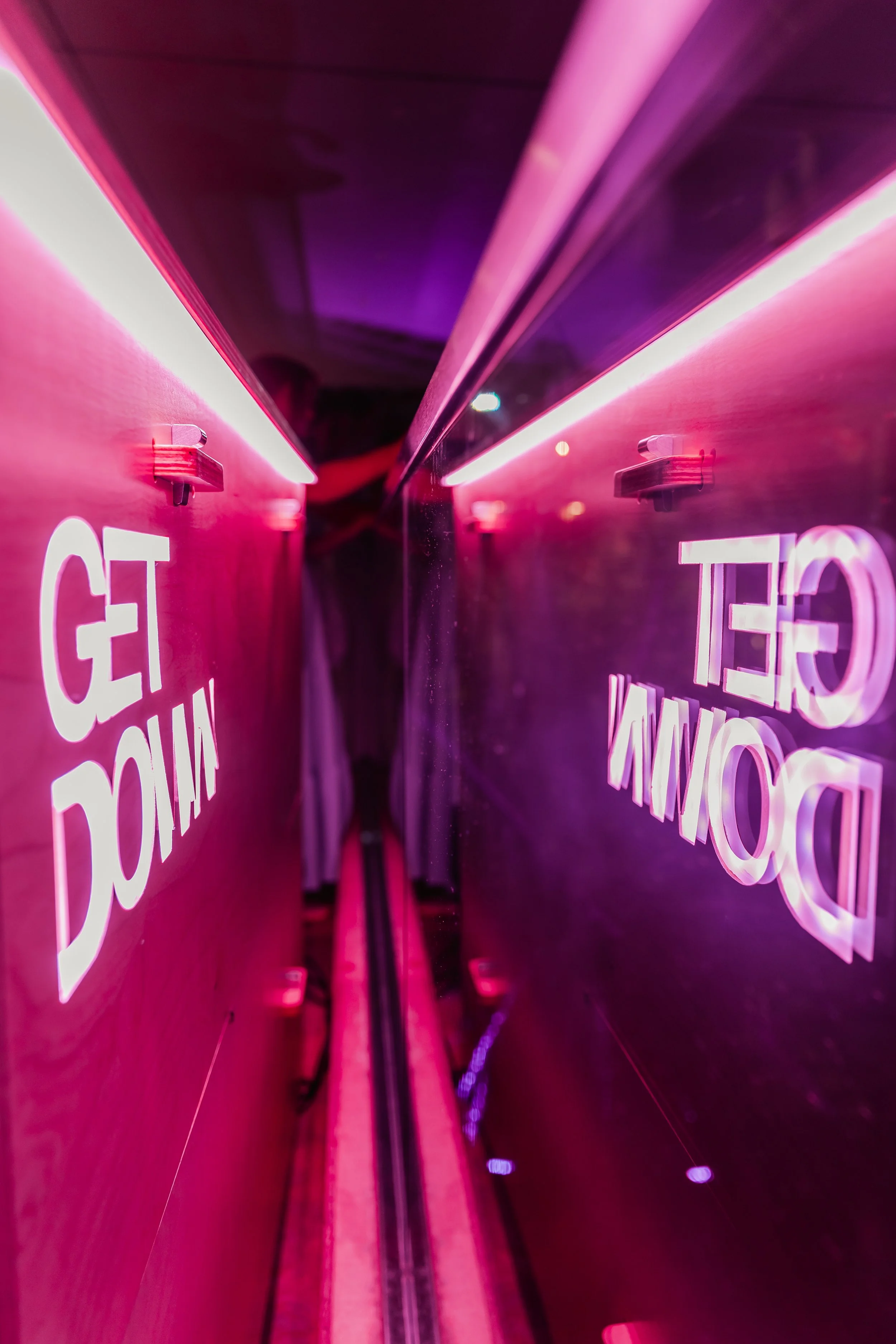 Pink neon sign that reads 'GET DOWN' reflected in a mirror.