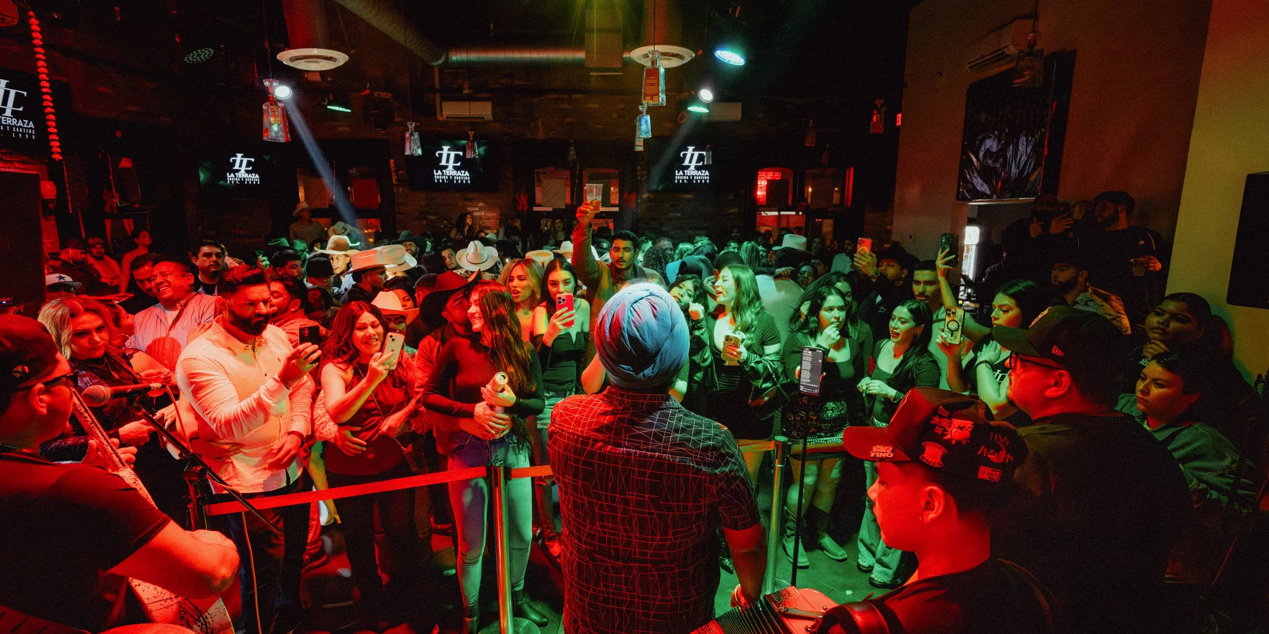 Crowd of people during a nightclub, in professionally lit venue, with a live Banda in the foreground.
