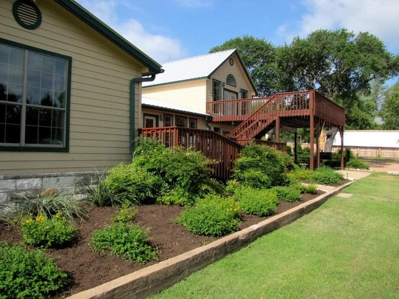 House with landscaped yard and wooden deck. Hill Country Texas lake cabin rentals.