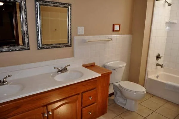 Bathroom with double sink vanity, mirrors, toilet, and bathtub with shower. Hill Country Texas lake cabin rentals.
