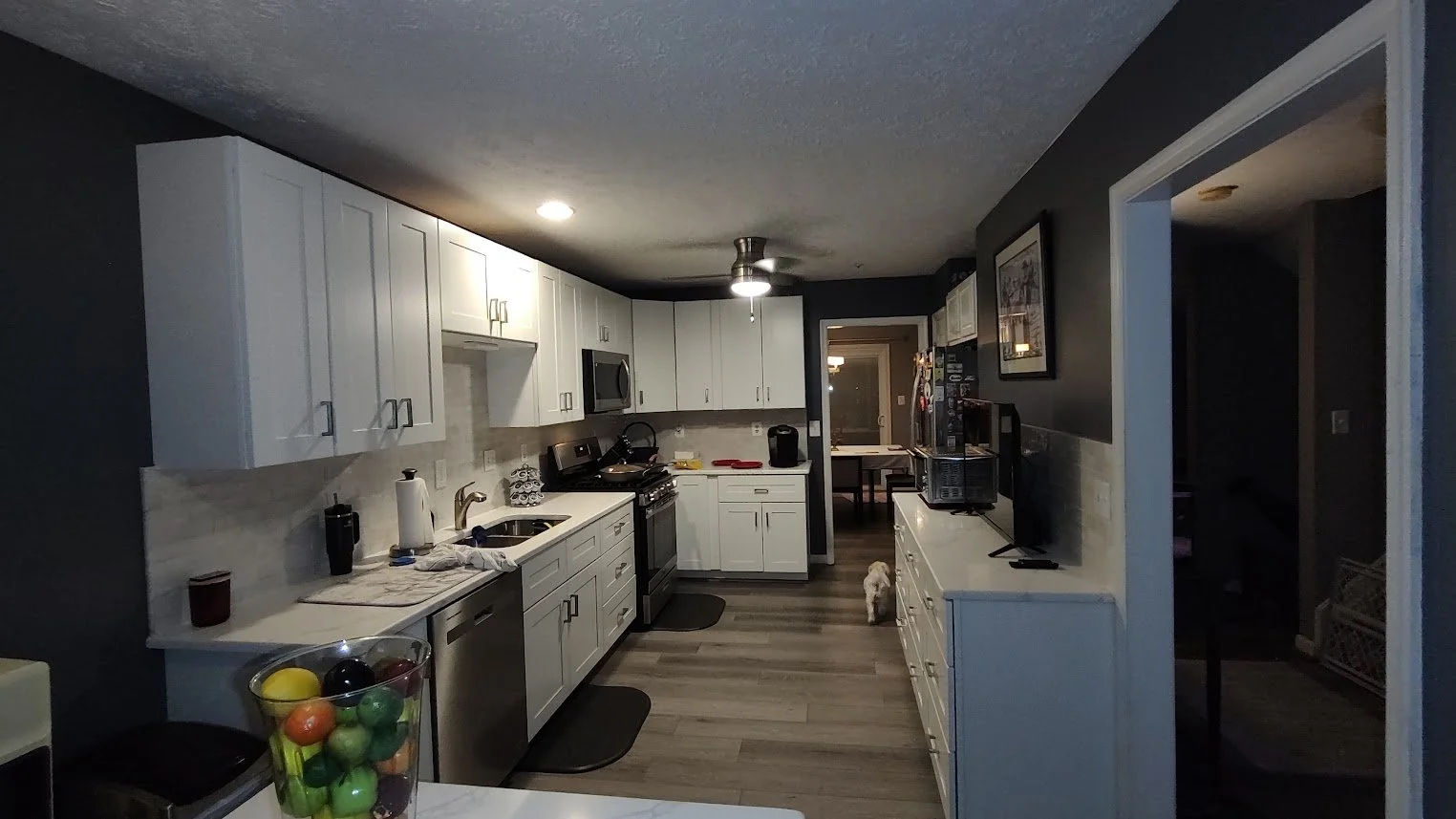 Completed kitchen with white cabinets, stone countertops, a tiled backsplash and wood-look flooring.
