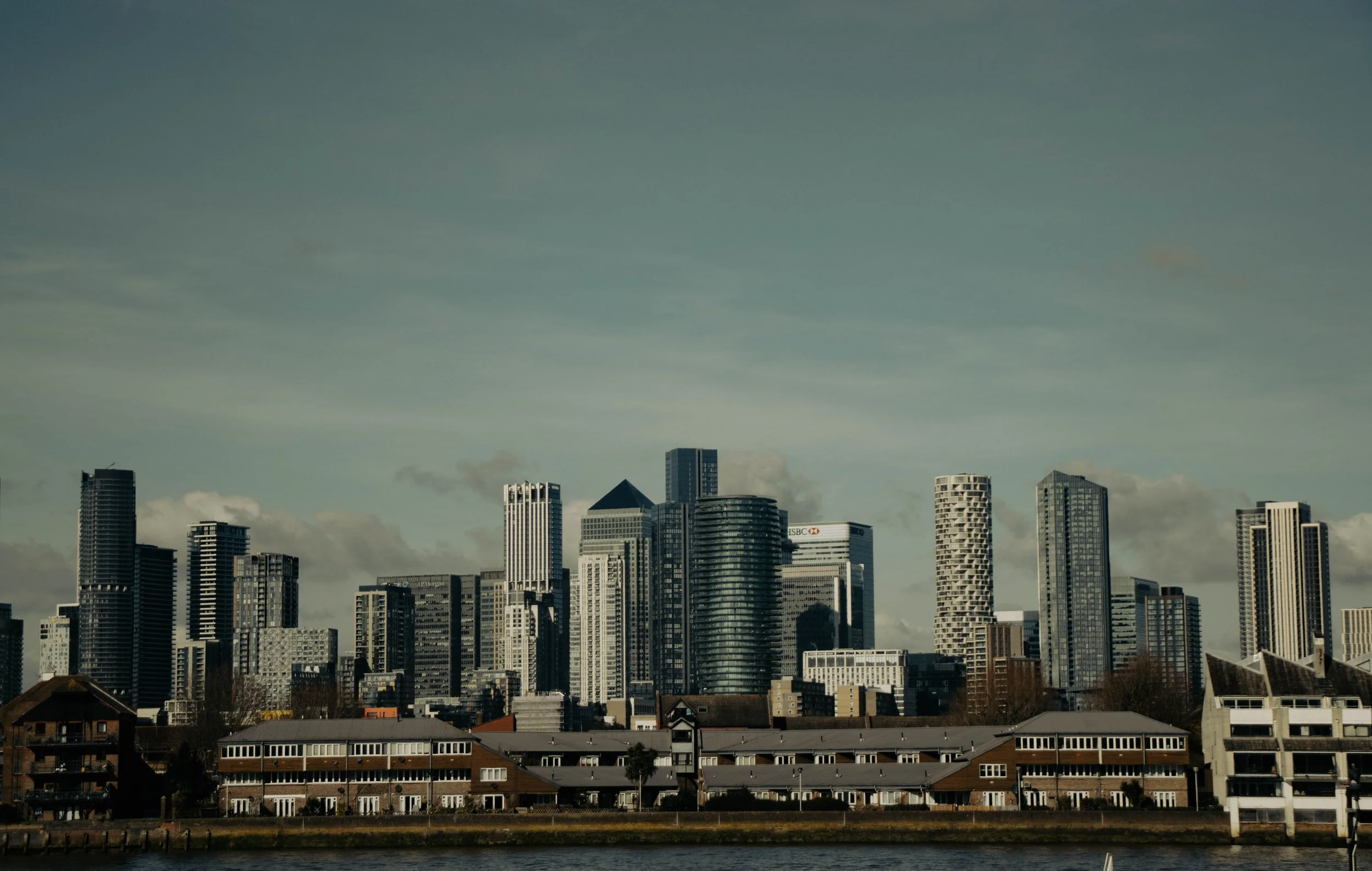 A city skyline with tall skyscrapers and buildings seen from across a body of water, with a clear sky above.