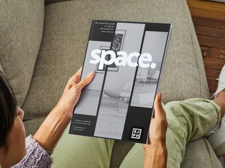 Persona seduta su un divano che tiene in mano un libro intitolato "Space" con immagini di interni di un appartamento sulla copertina.