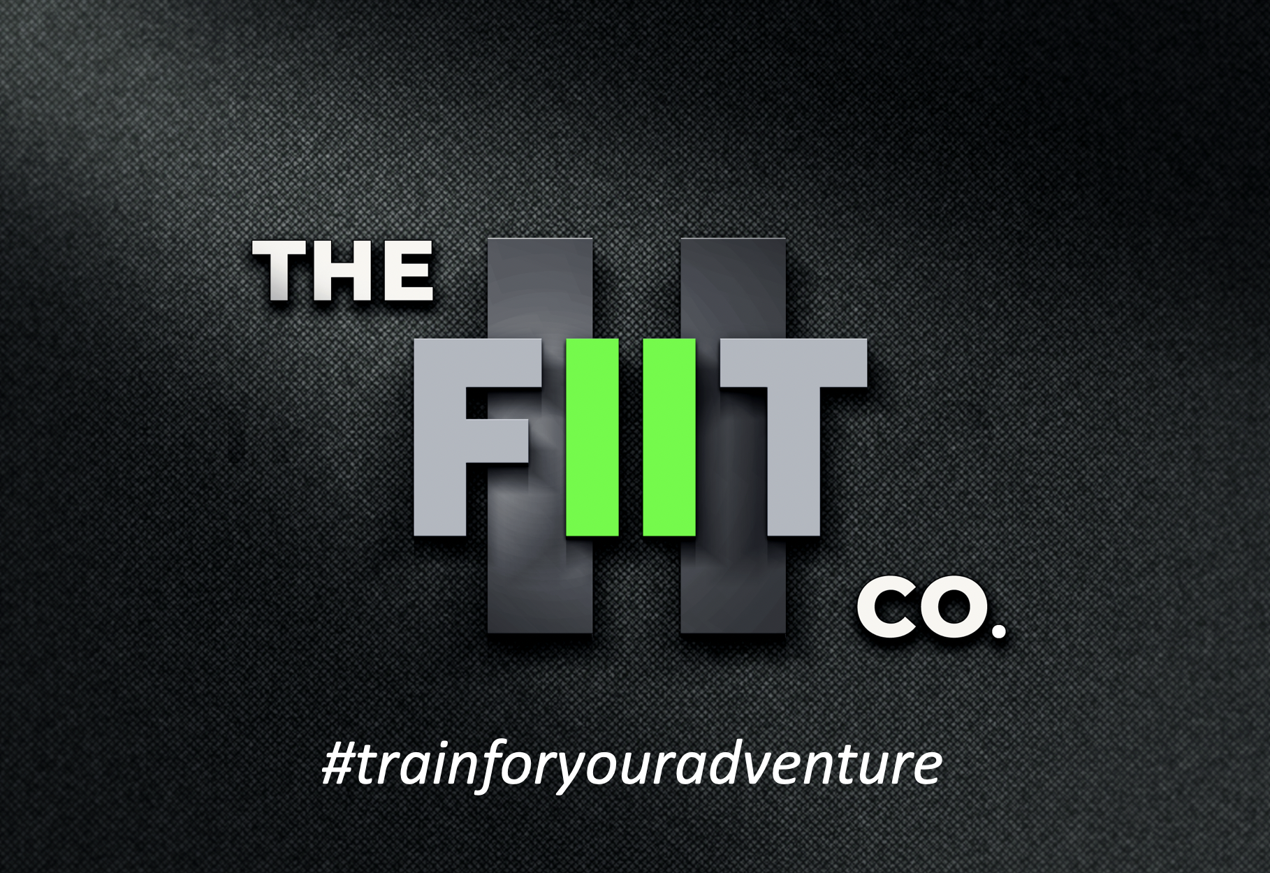 Logo for 'The Fit Co.' featuring stylized text with green and gray bars in the background on a dark textured surface. The hashtag '#trainforyouradventure' is at the bottom.