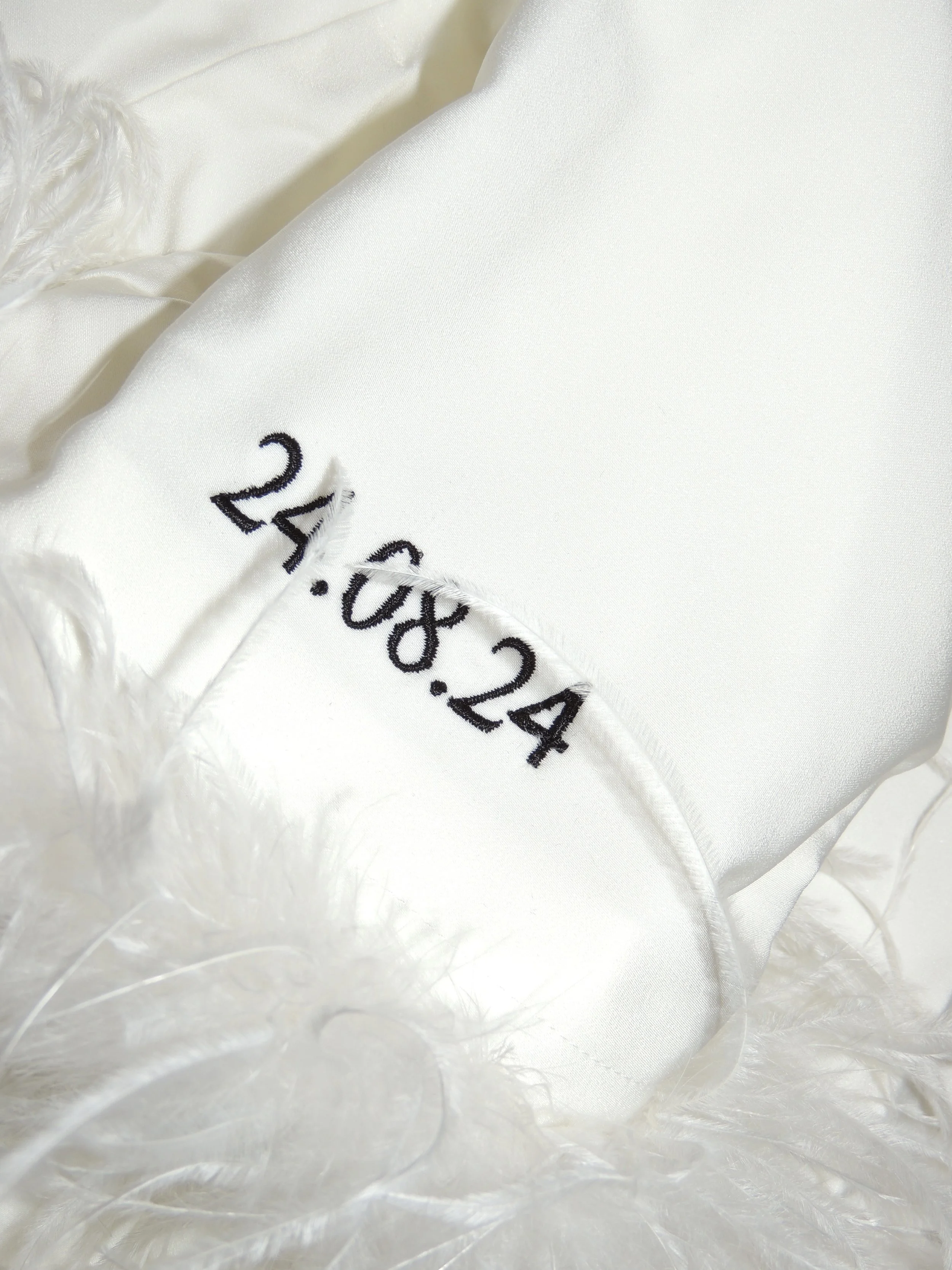 White fabric with embroidered date "24.08.24" and feather trim