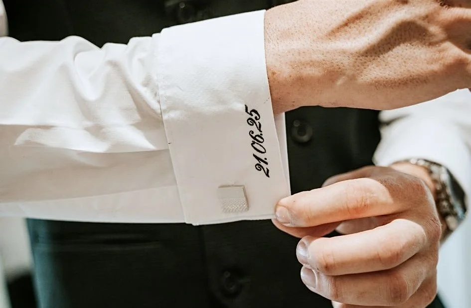 Close-up of a person adjusting a white dress shirt cuff with a date written on it, 21/08/25.