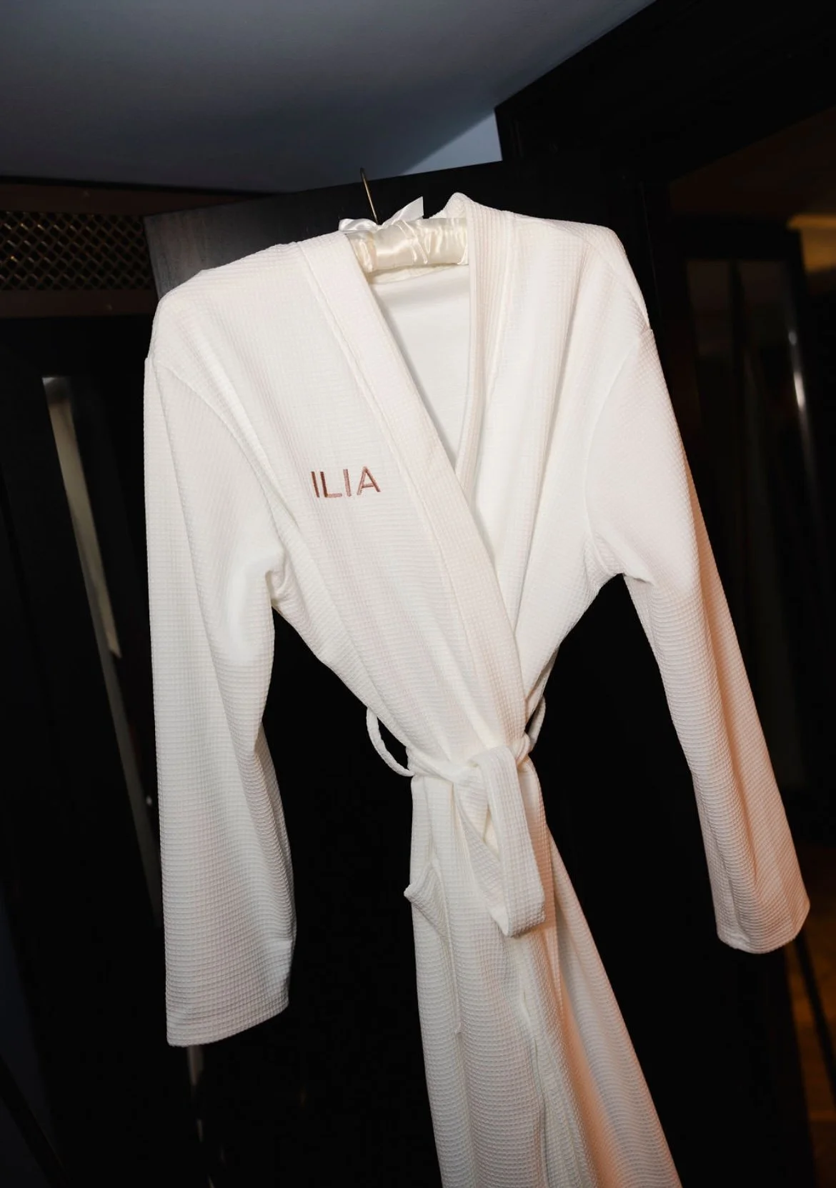 White embroidered martial arts gi with the name 'ILIA' on the front pocket, hanging on a hanger.
