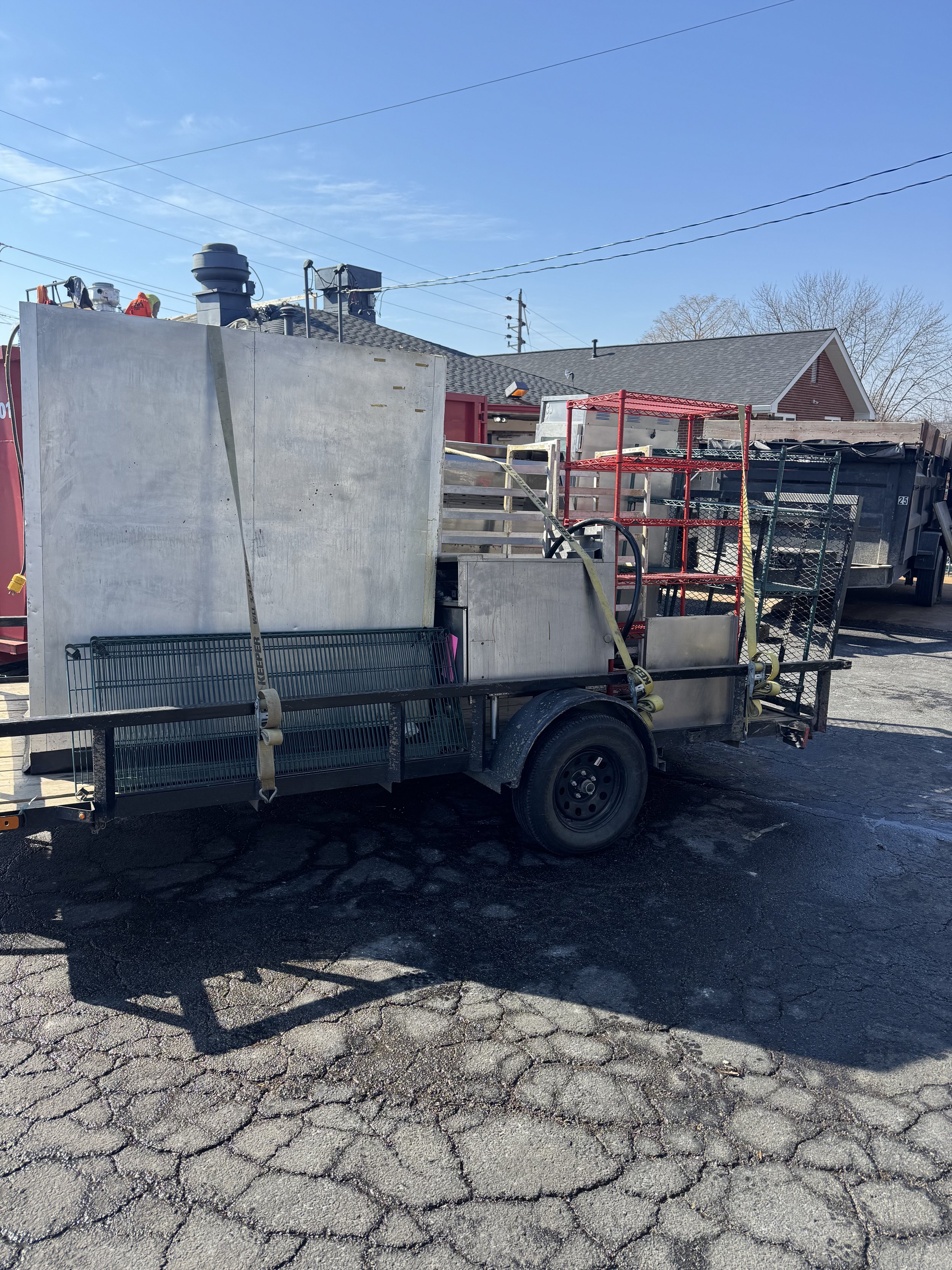 A trailer loaded with metal shelves, equipment, and construction tools in a business parking lot. Heavy commercial grade appliances loaded onto the trailer