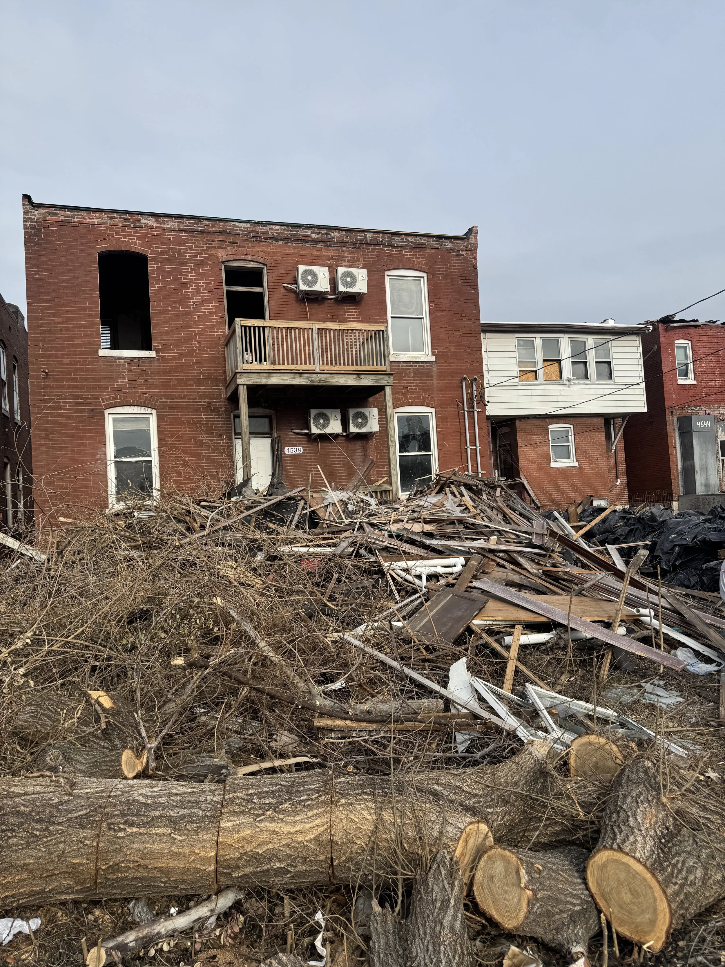 A damaged brick building with debris and fallen trees in the foreground.