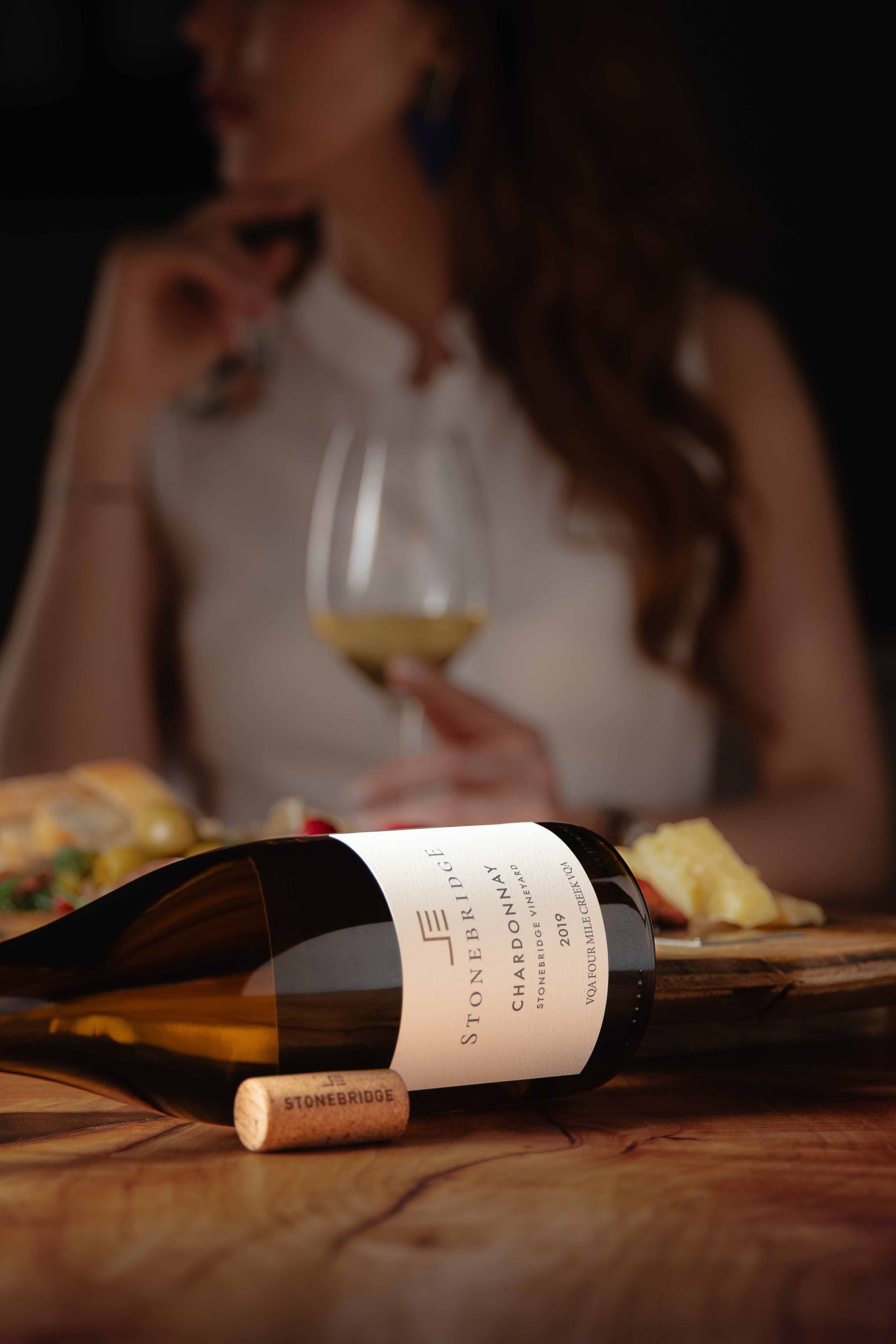 A bottle of Stonebridge wine with a woman holding a wine glass in the background