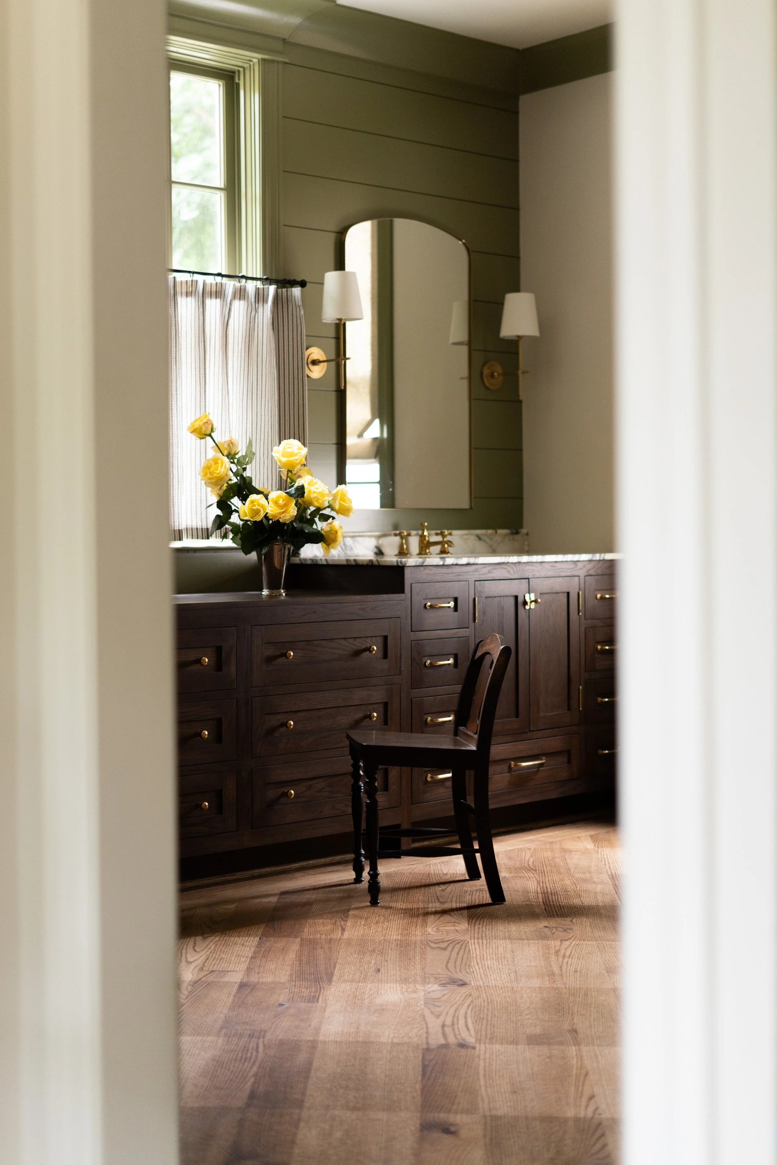 A bathroom vanity with dark wood cabinetry, a white marble countertop, a yellow rose bouquet, a large mirror, and two wall-mounted white lamps.