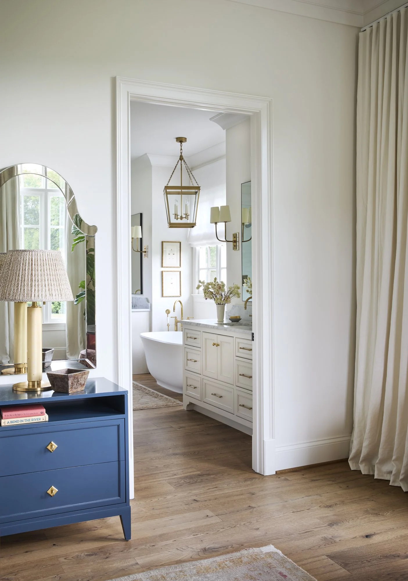 A view through an open doorway into a bathroom with a freestanding bathtub, a vanity with a marble top, and a chandelier.