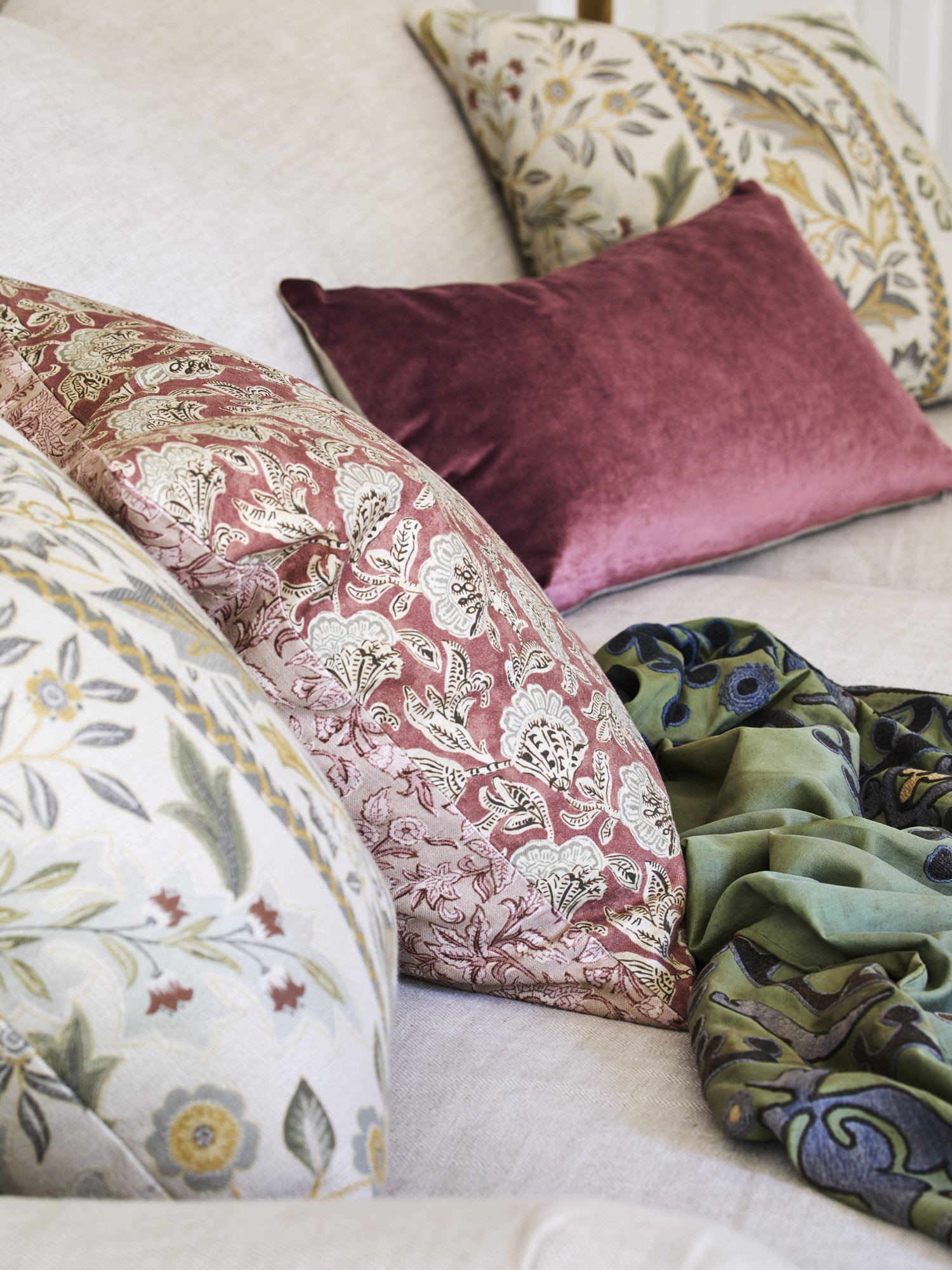Decorative pillows in floral and plain designs on a cream-colored sofa with a matching floral pillow and a green and black patterned throw blanket.