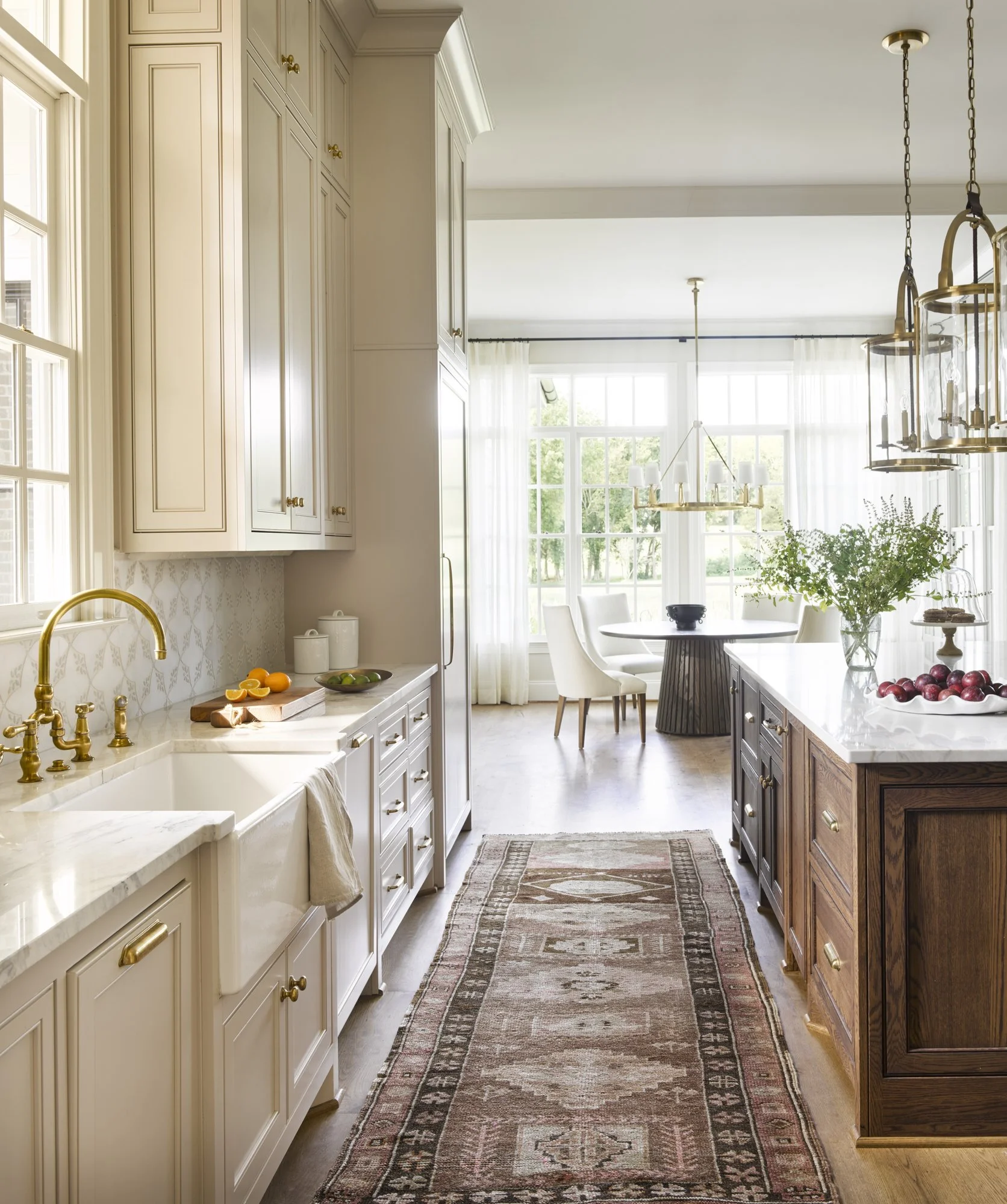 Bright kitchen with white cabinets, a wooden island, gold fixtures, and a dining area with large windows and sheer curtains.