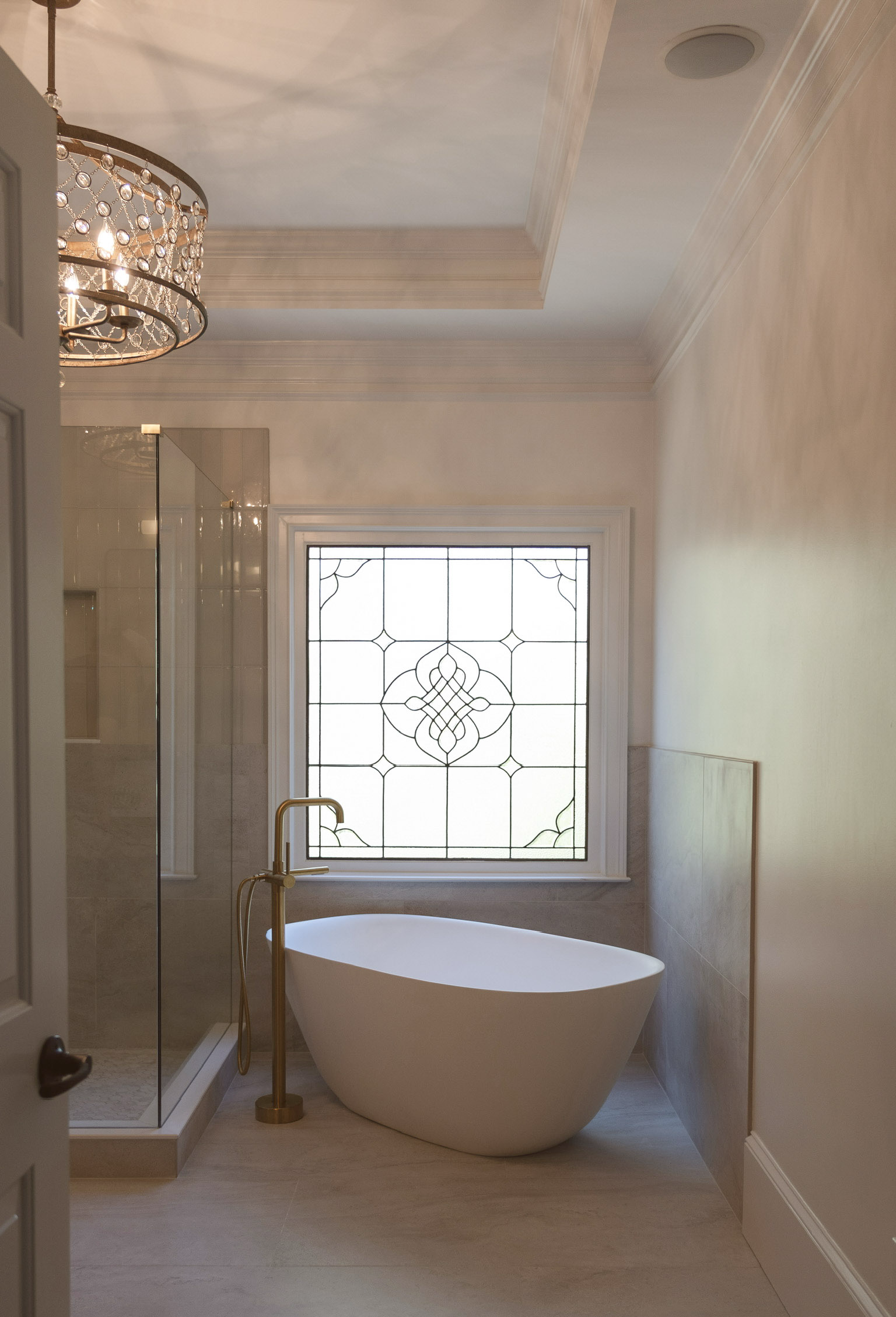 Bathroom with freestanding soaking tub, stained-glass window, glass shower enclosure, and brass floor-mounted faucet.
