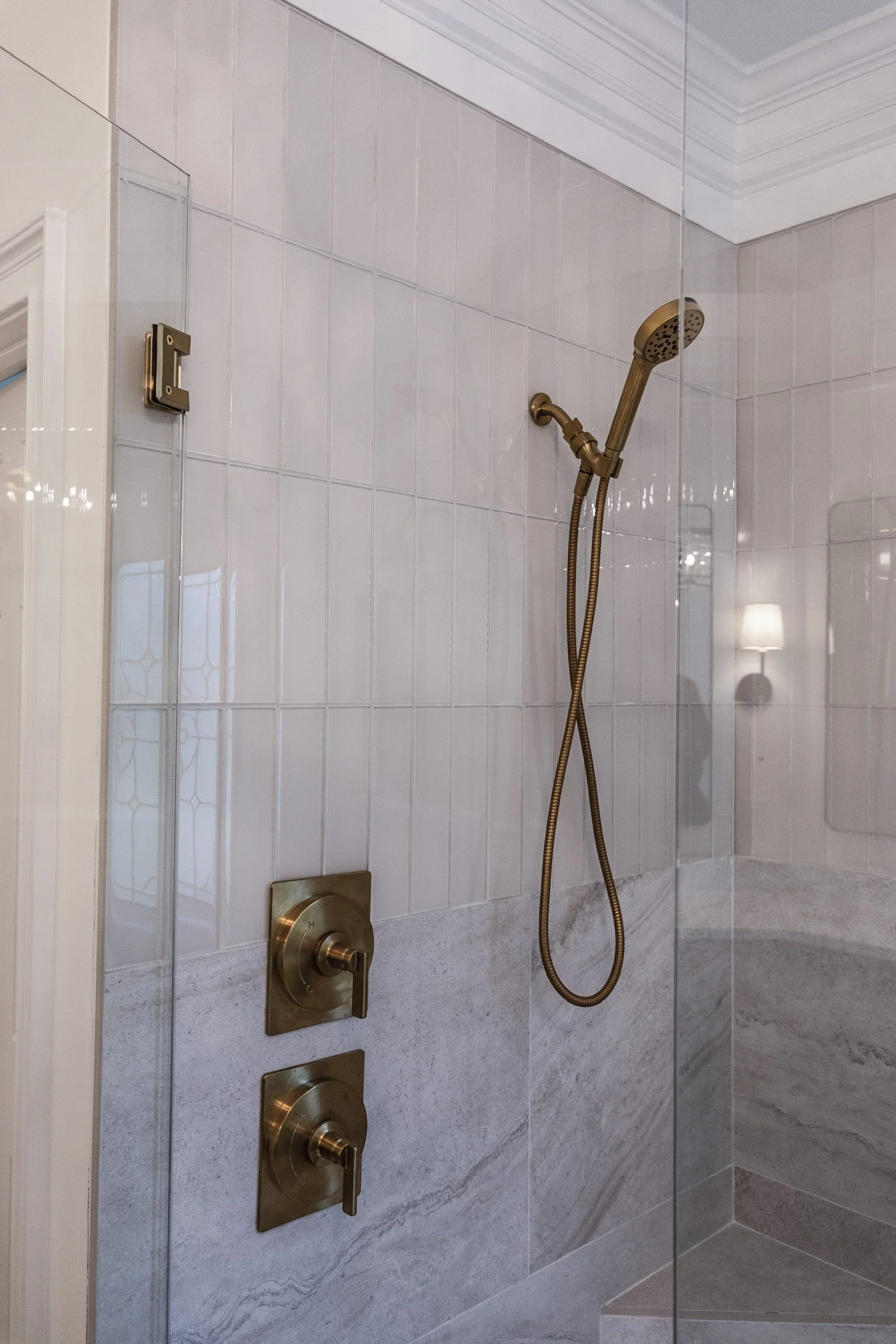 Walk-in shower with marble-look tile walls, glass enclosure, and brass shower fixtures.