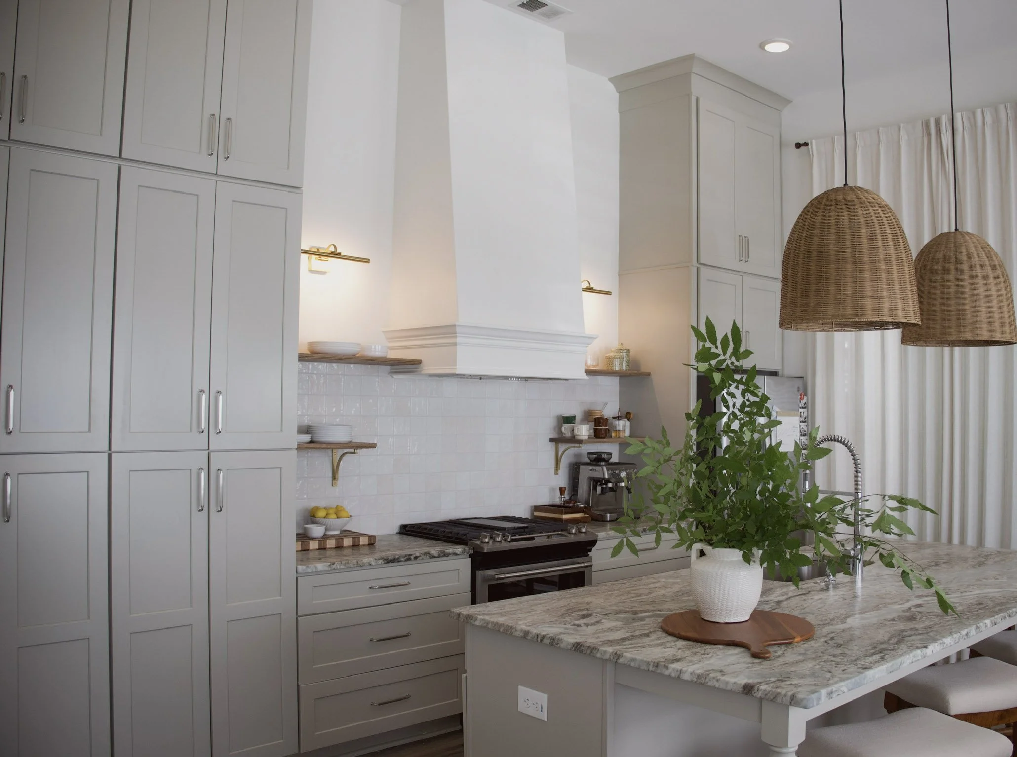Modern kitchen with custom cabinetry, stone island, statement range hood, and woven pendant lighting.