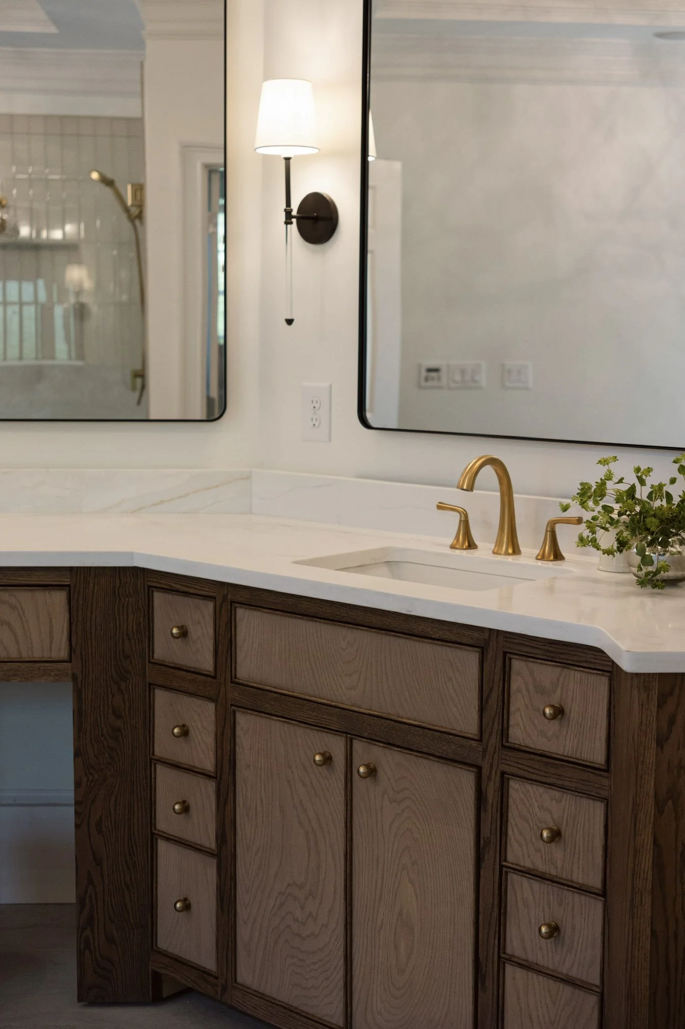 Bathroom vanity with dark wood cabinetry, stone countertop, brass faucet, and wall-mounted mirror.