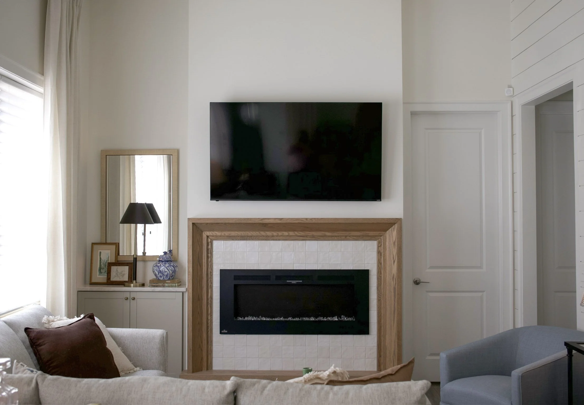 Living room with wall-mounted TV, fireplace, light wood mantel, built-in cabinetry, and neutral furnishings.