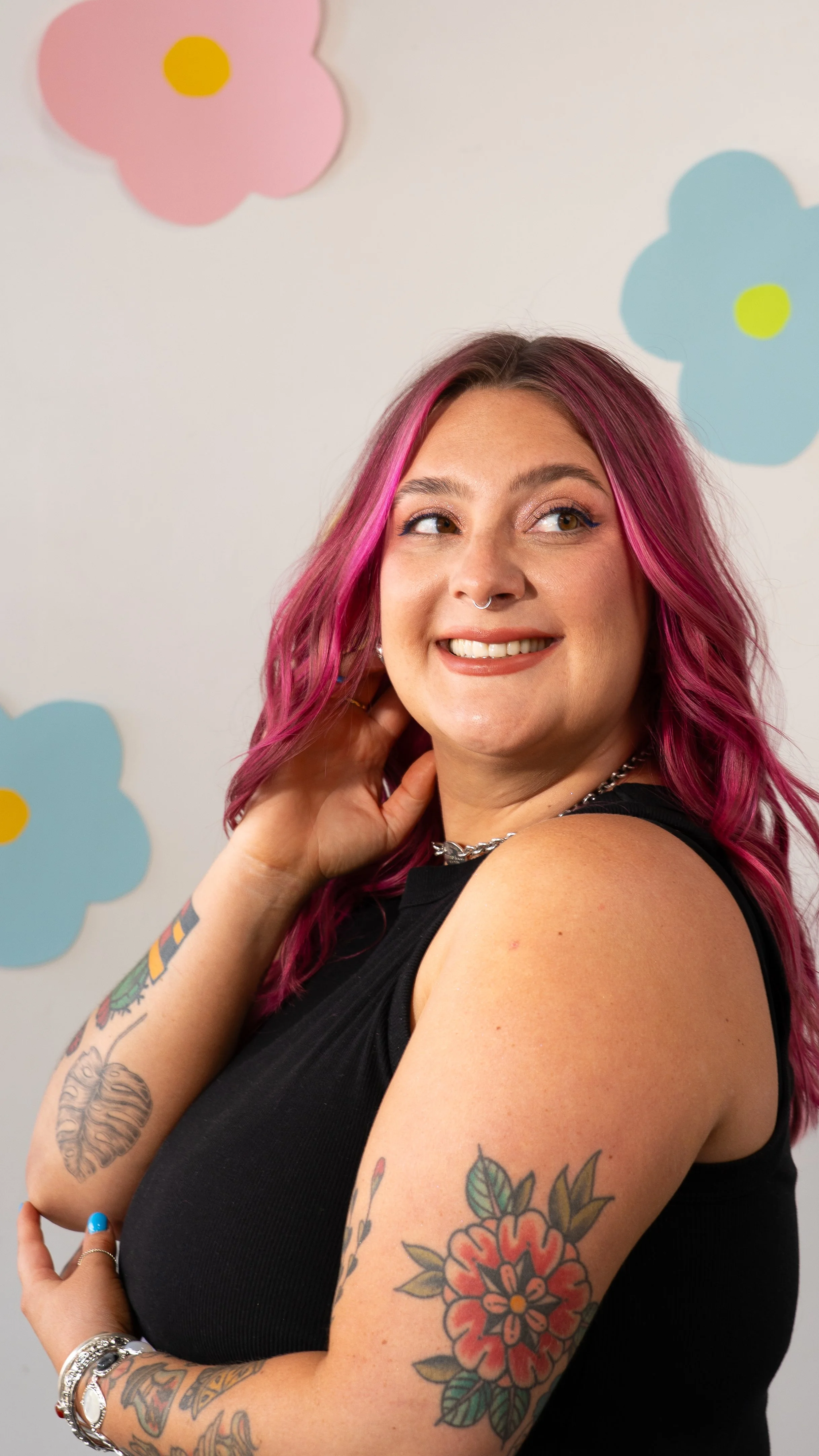 Cid from Honey Bee Color Collective with long magenta hair, smiling over her shoulder in front of a daisy-print wall.