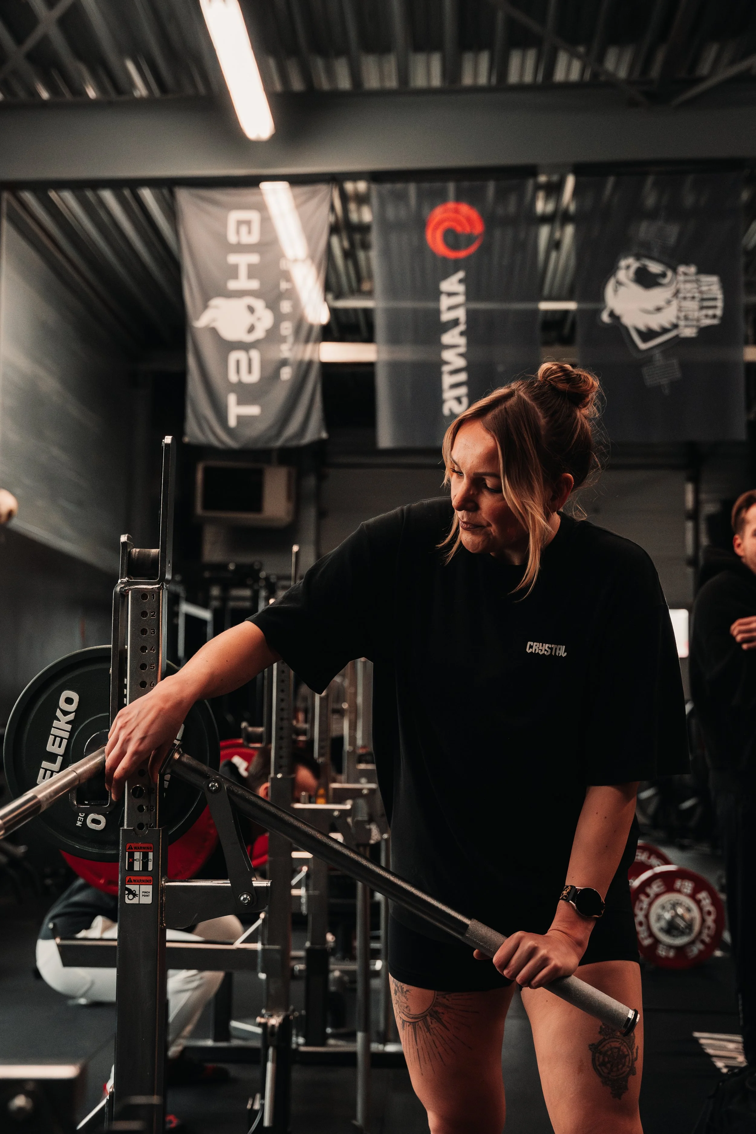 Vrouw die fitnessapparatuur afstelt in een sportschool, staand naast een halterrek met gewichten.