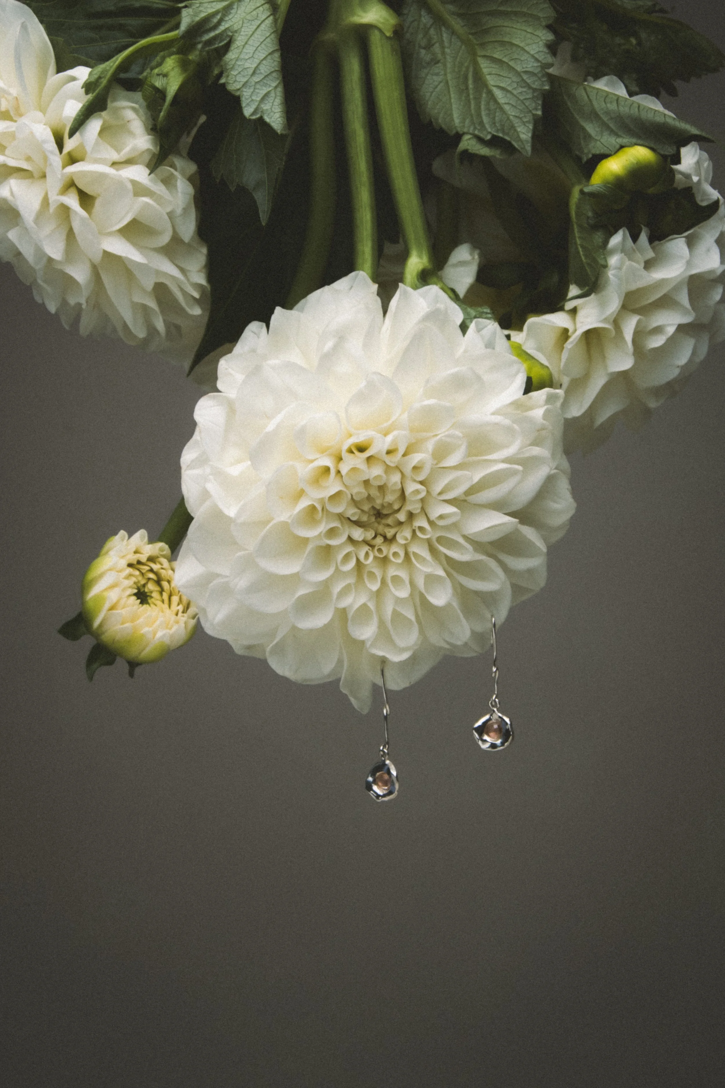 White dahlias with dangling white gold earrings hanging from a flower in a floral arrangement.