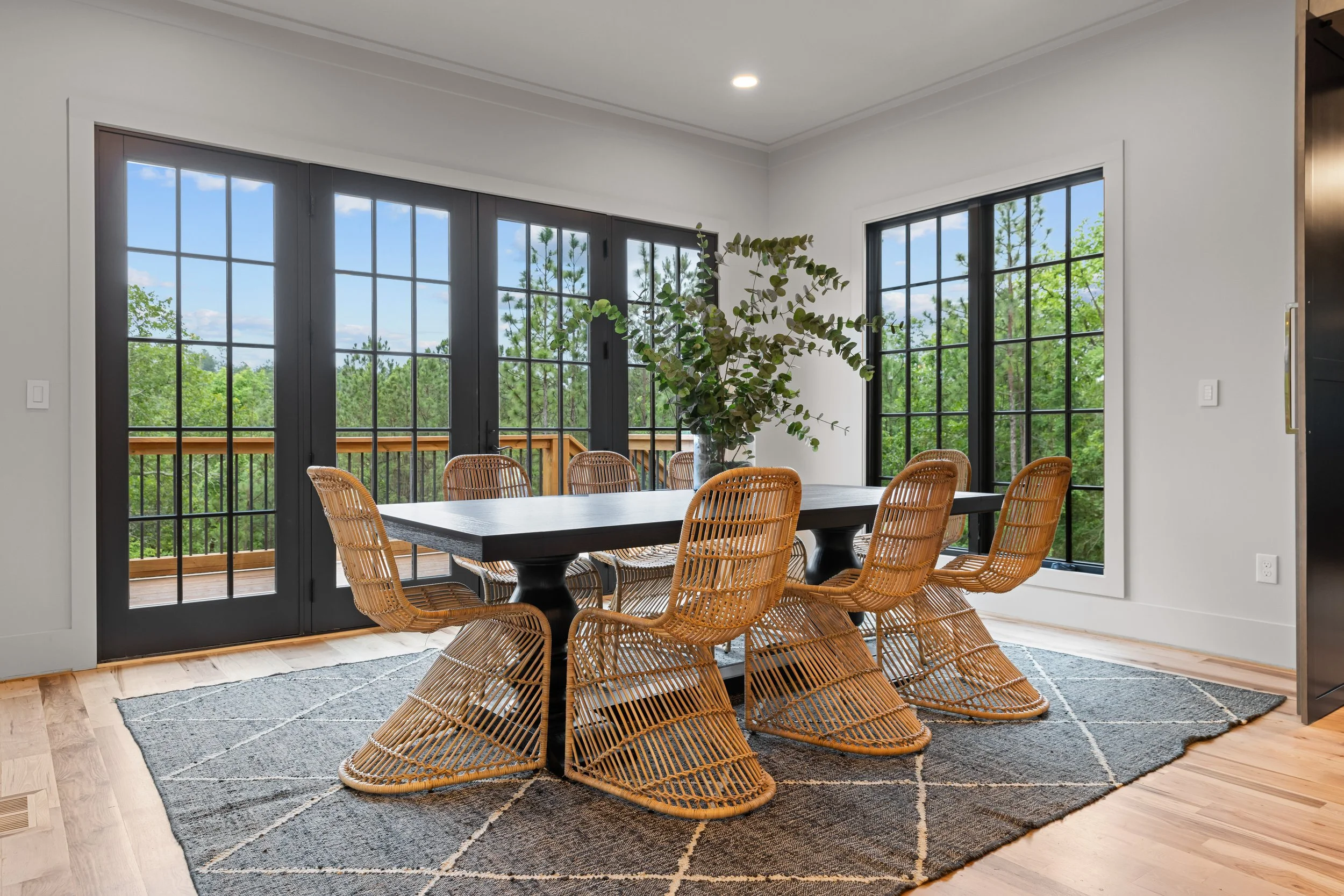 Dining room with a black table, rattan chairs, large windows, and a potted plant