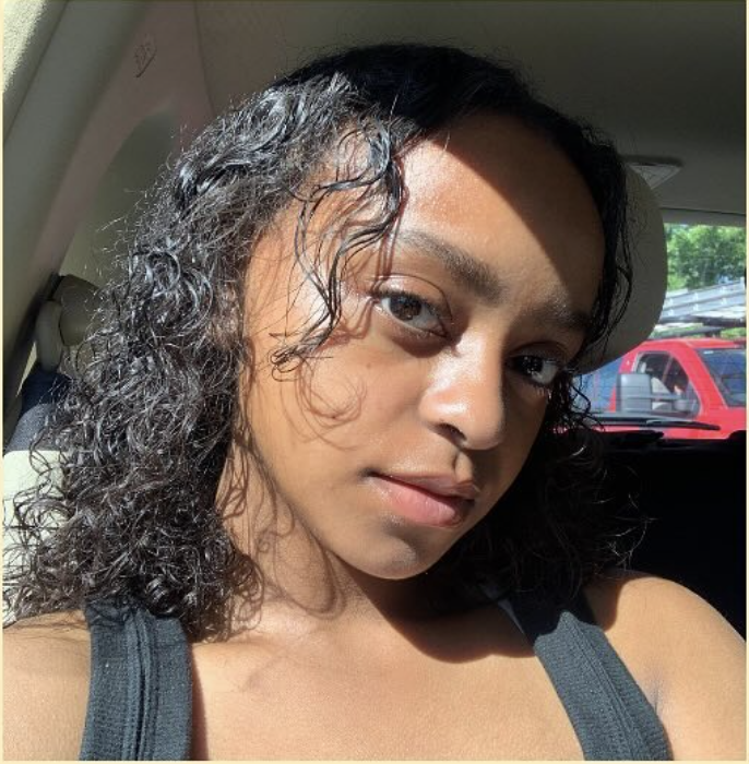 Person with curly hair sitting in a car, sunlight on their face