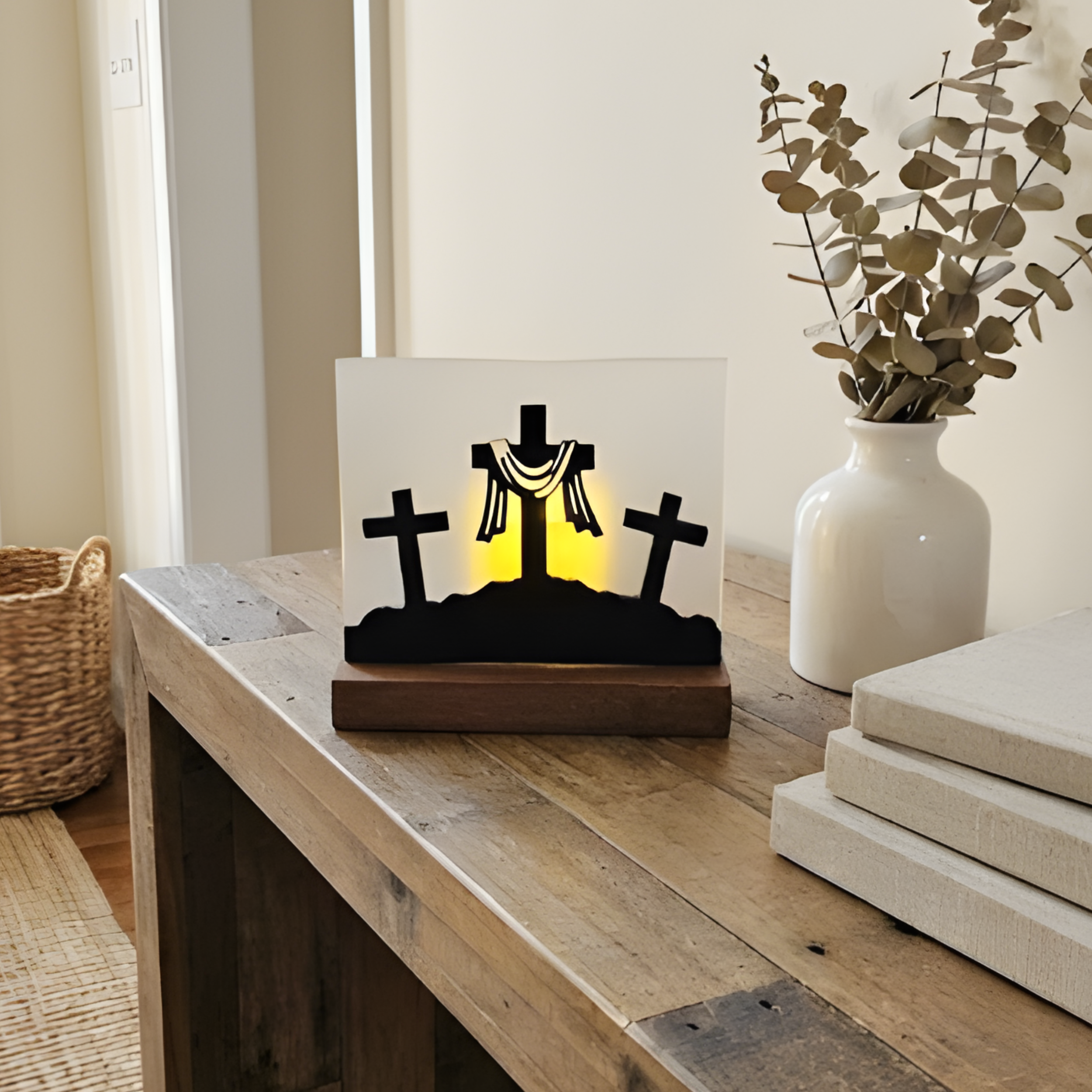 Calvary cross silhouette art with dark walnut base styled on a shelf with a vase and books.