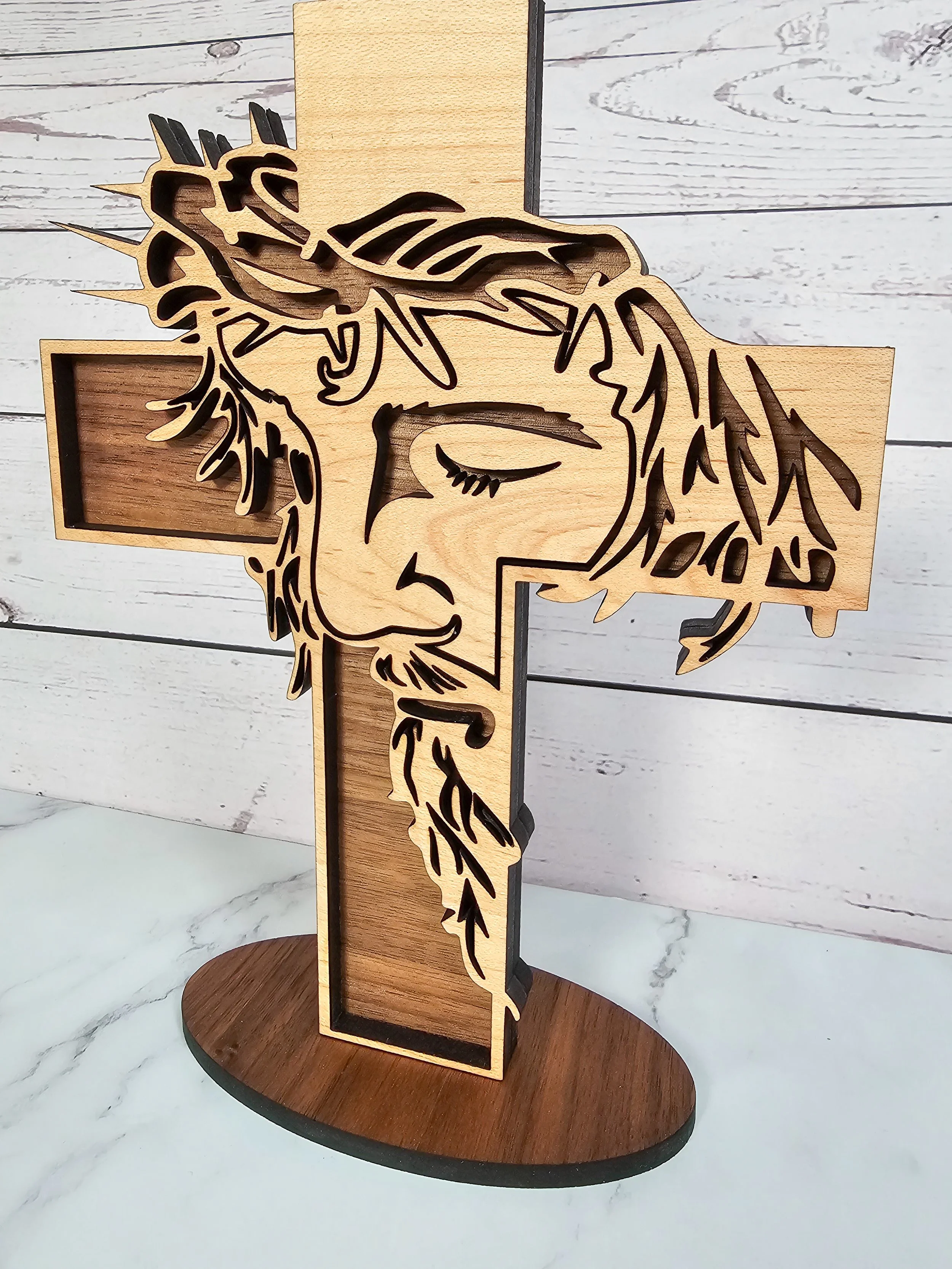 Close-up detail of laser-cut crown of thorns and facial features on a maple and walnut wood cross.