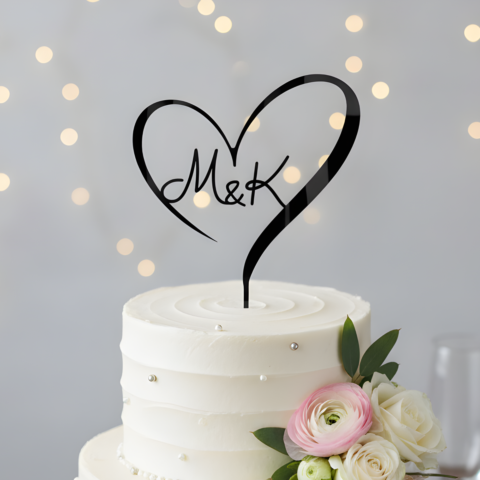 Sleek black personalized heart initial cake topper for "M&K" on a white frosted wedding cake.