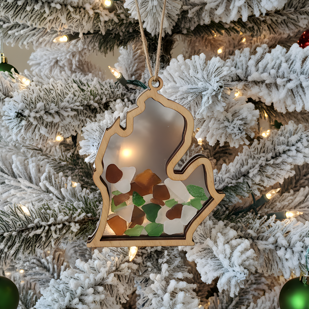 Michigan mitt wood ornament with frosted backing catching tree light behind coastal treasures.