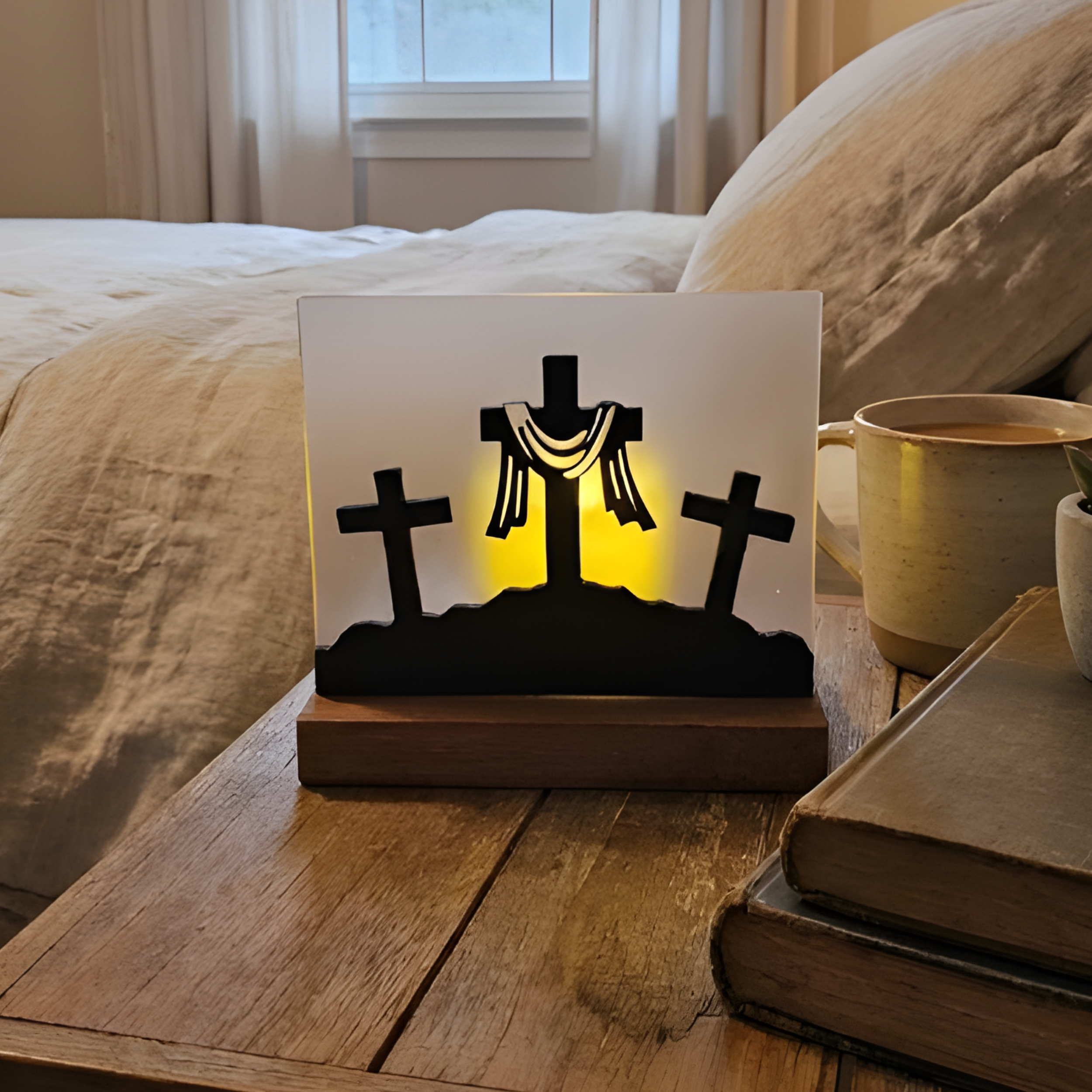 Illuminated Calvary cross scene with three crosses on a wood base on a nightstand with coffee and books.