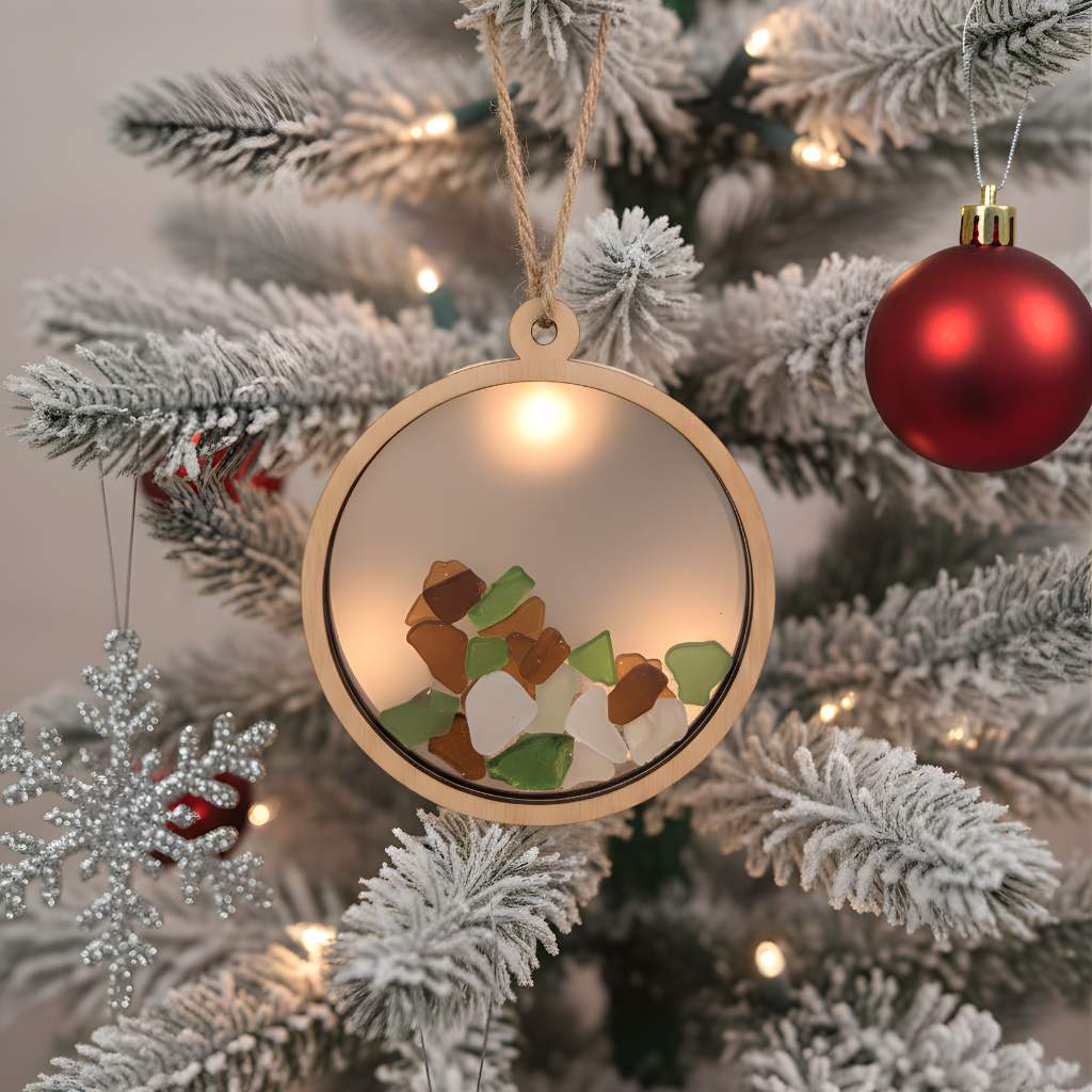 Coastal treasure ornament filled with multi-colored sea glass hanging on a frosted holiday tree.