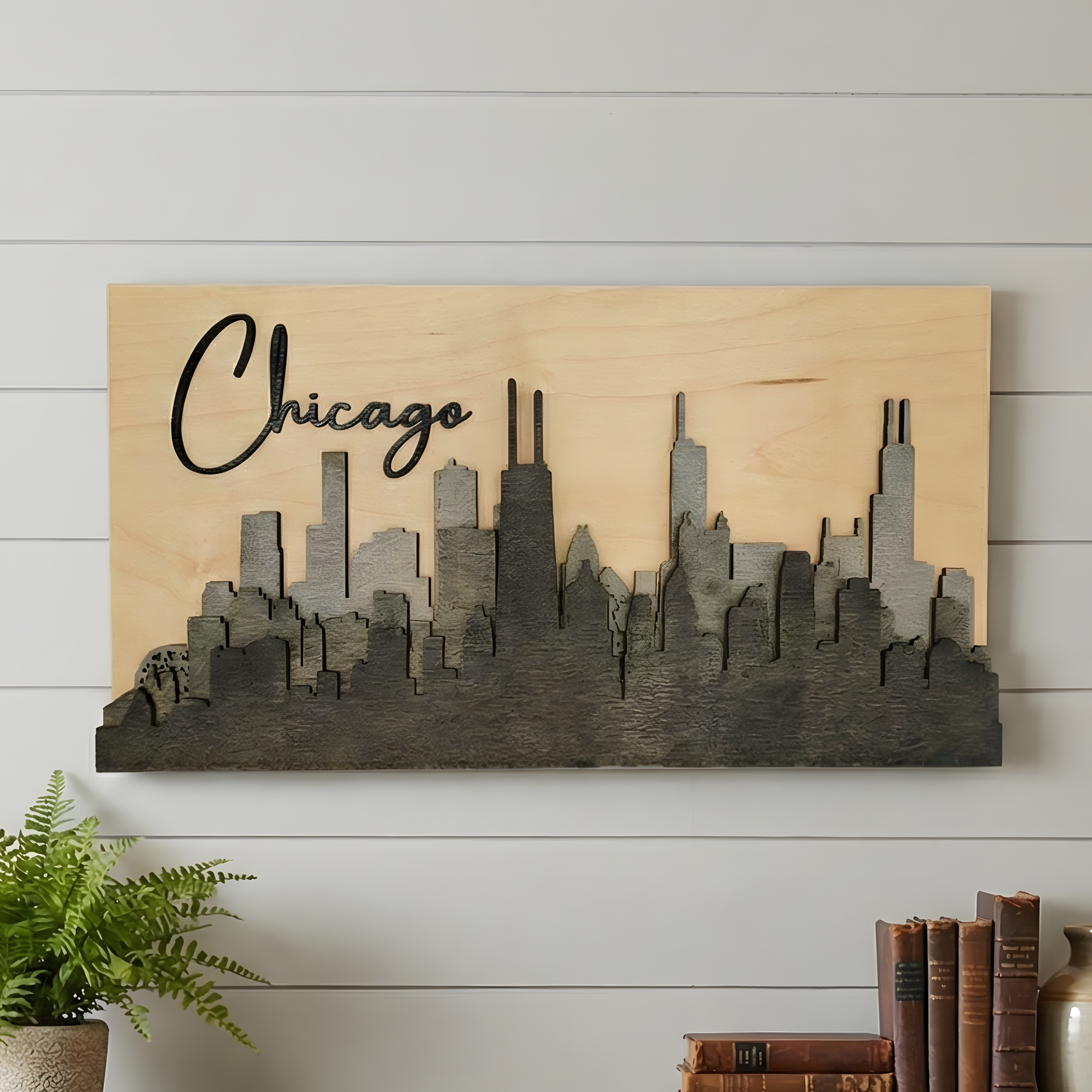 3D grey Chicago wood skyline art hanging on a white shiplap wall with plants and books.