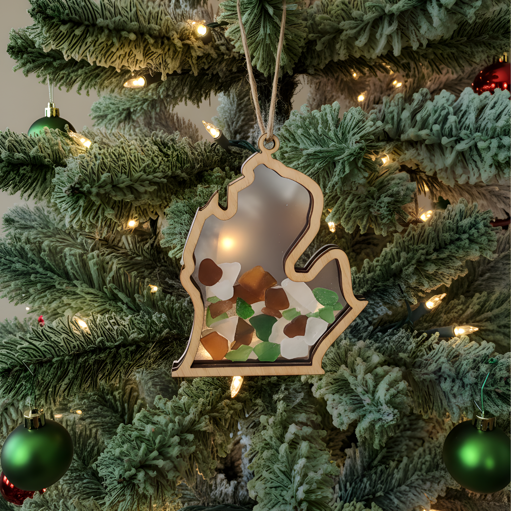 Handcrafted Michigan-shaped wood ornament filled with green and brown beach glass on a frosted holiday tree.