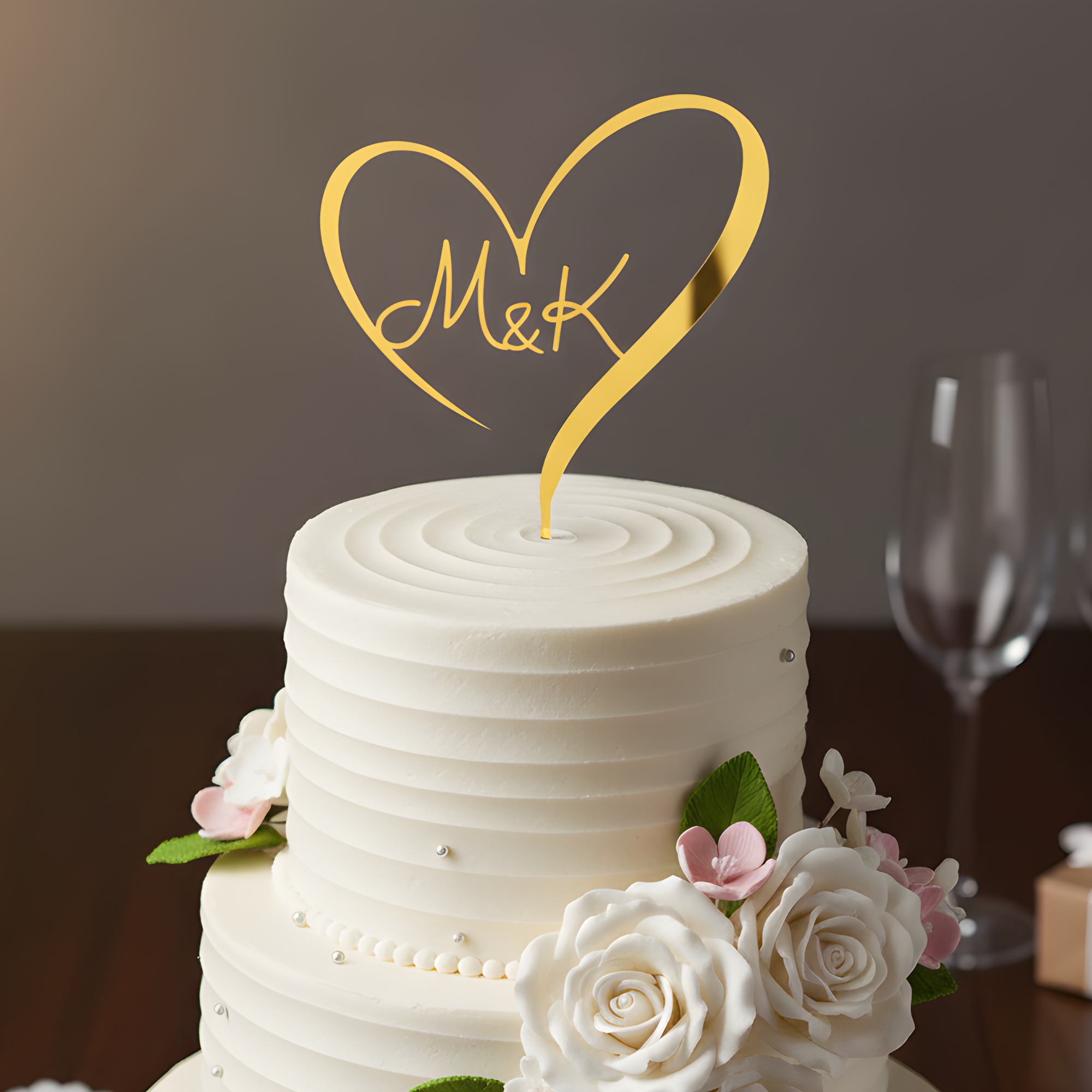 Gold mirrored acrylic heart wedding cake topper with initials "M&K" on a white cake with white roses.