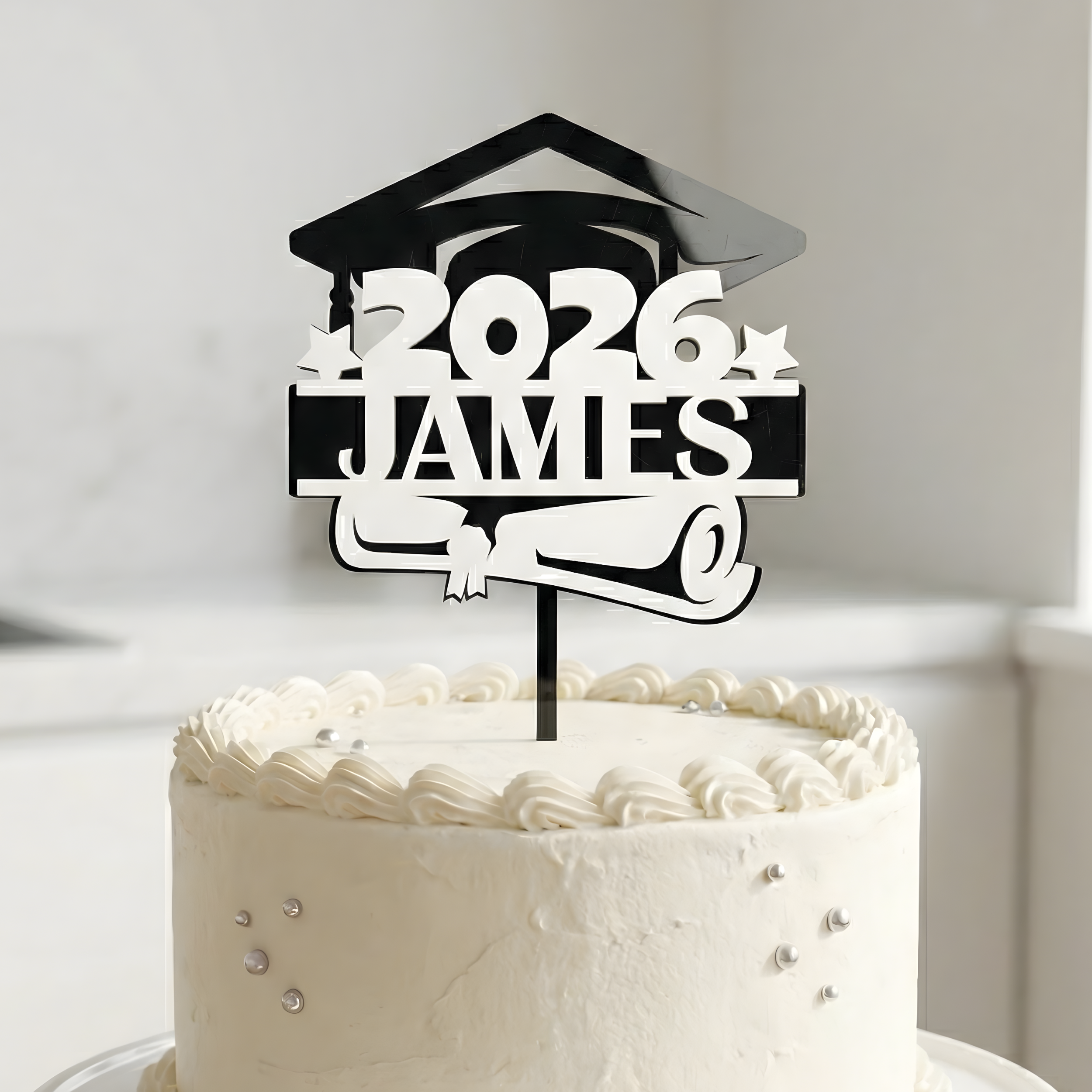 Sleek black and white personalized graduation cake topper for "James" 2026 on a tiered white cake.