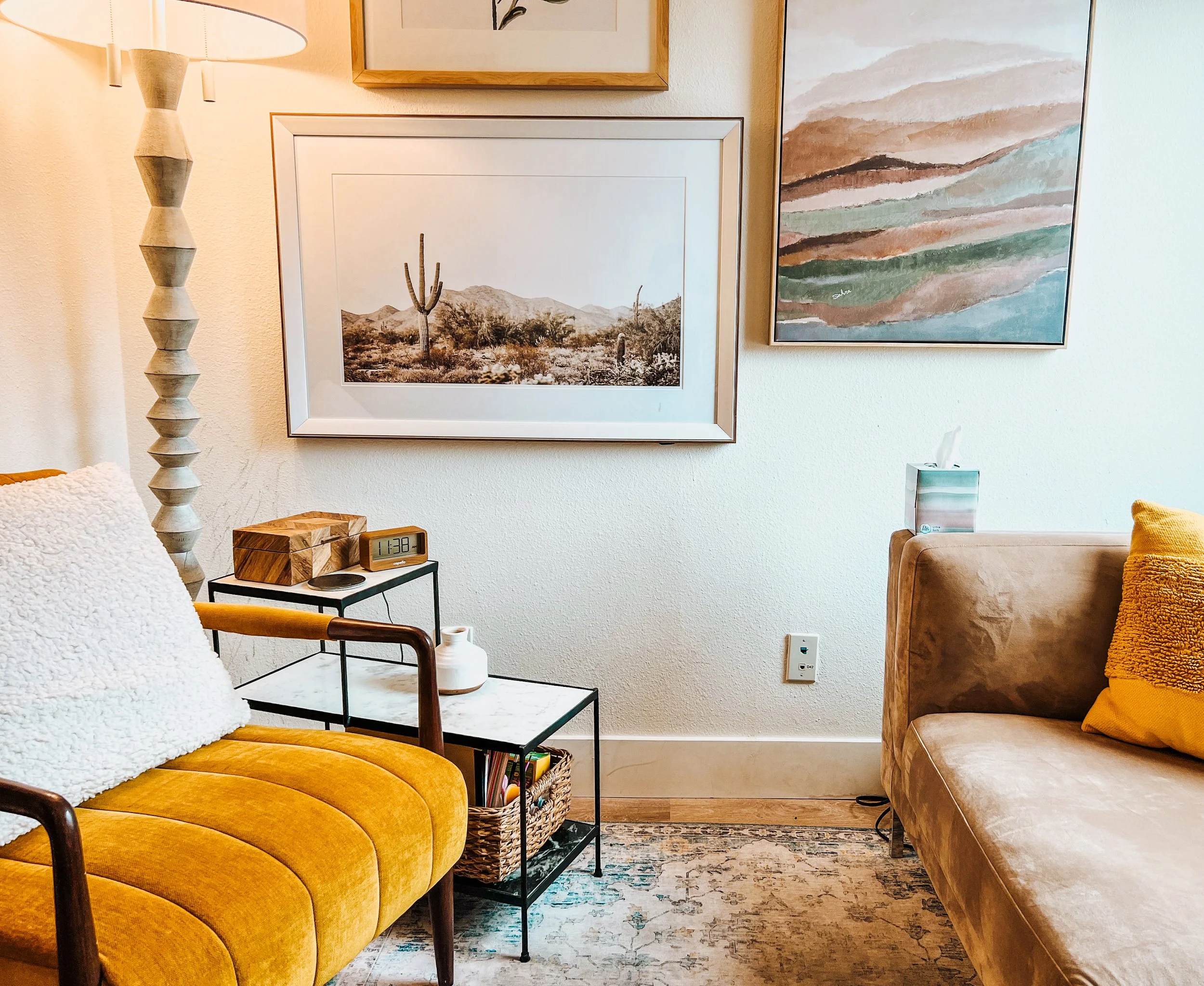 Cozy living room with yellow armchair, decorative floor lamp, framed wall art, beige couch with yellow pillow, side table with clock and vase, tissue box on couch, and decorative rug.