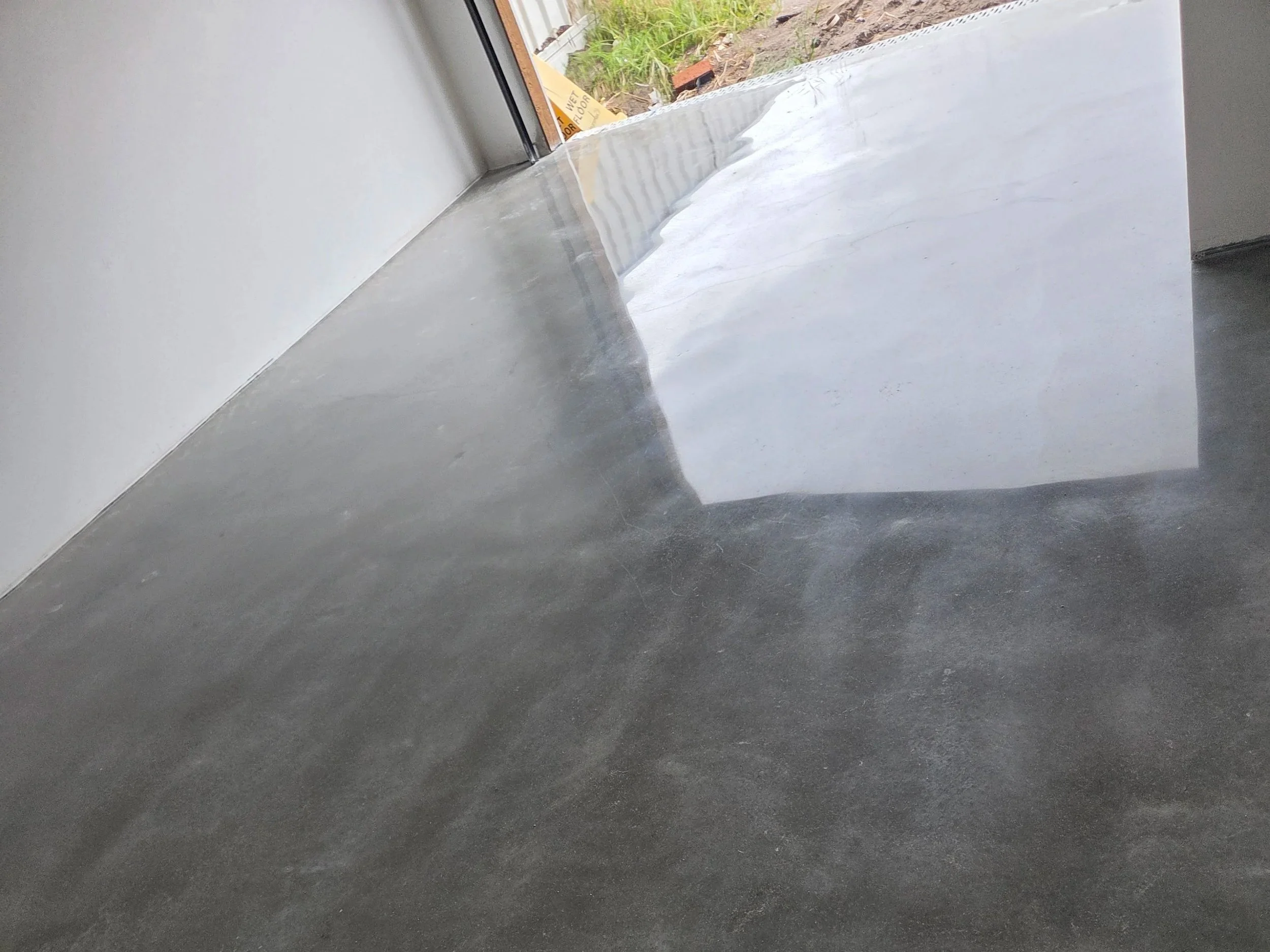 Empty concrete floor with a white paper partially visible at the edge, an open door leading outside to a grassy area.