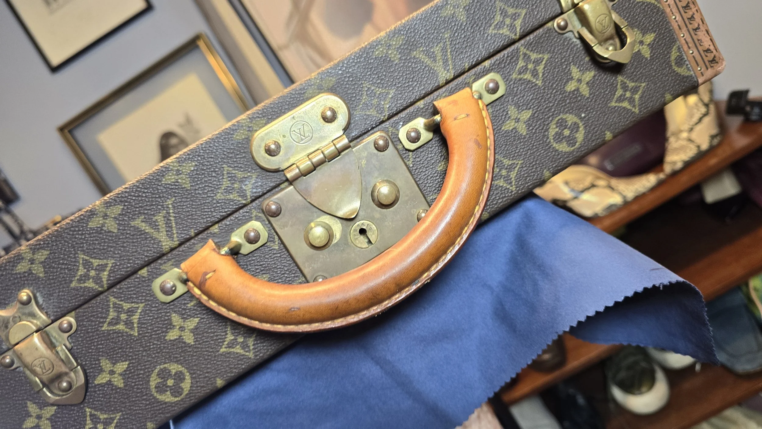A vintage Louis Vuitton trunk with a monogram pattern, brass hardware, and a leather handle.