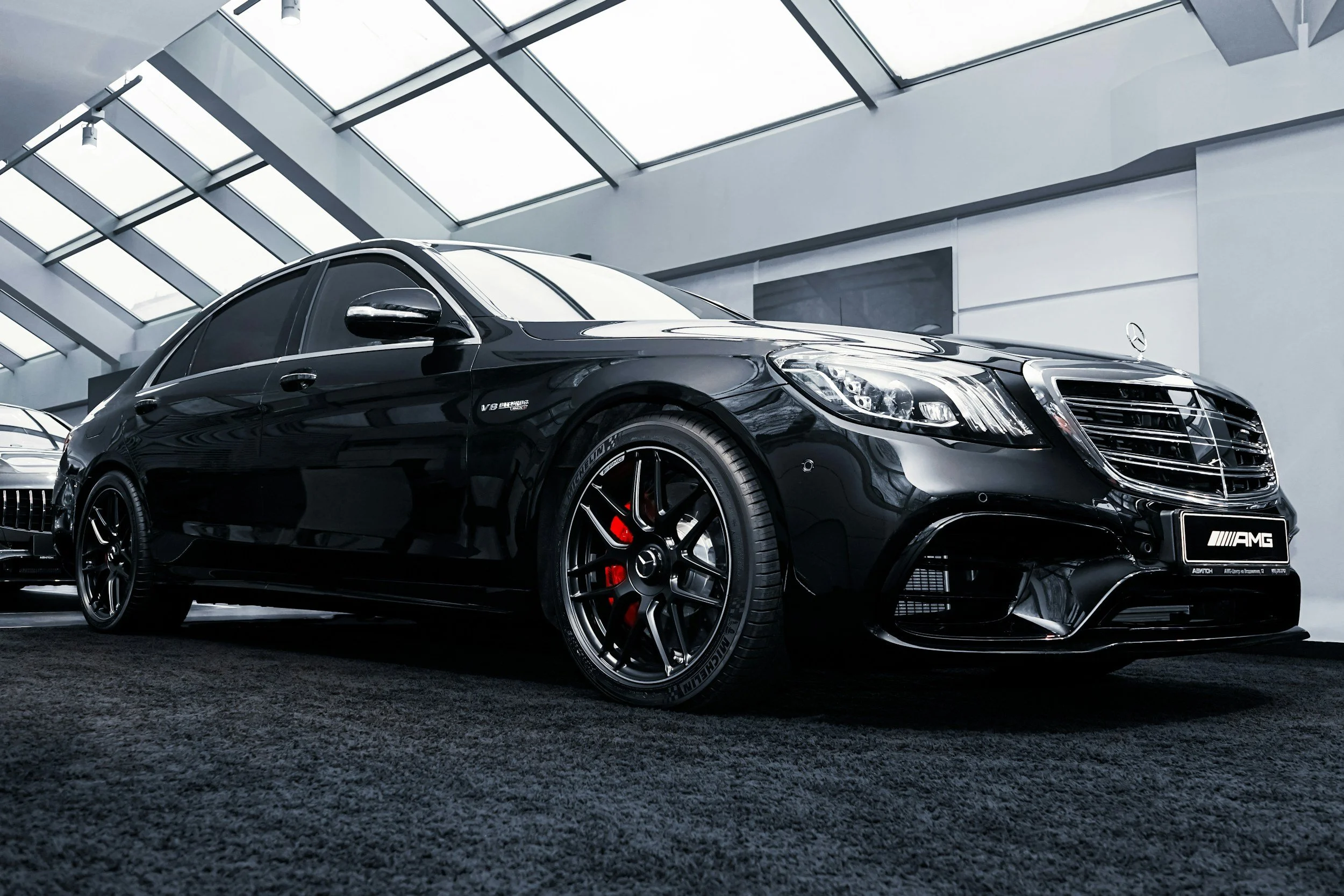 Luxury black Mercedes-AMG sedan with chrome details on display in a modern showroom with large windows.