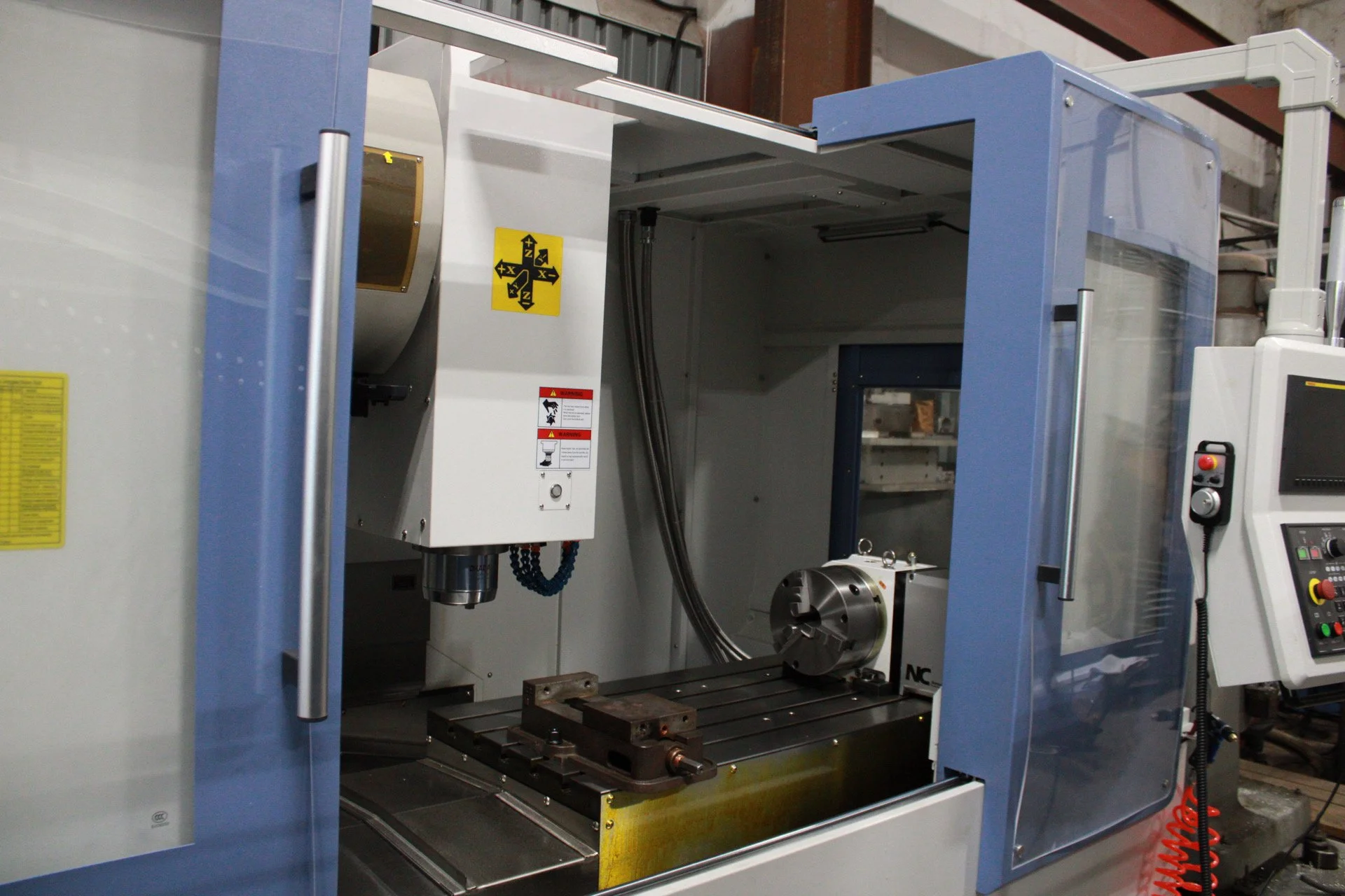 CNC milling machine with open door showing control panel and worktable inside.