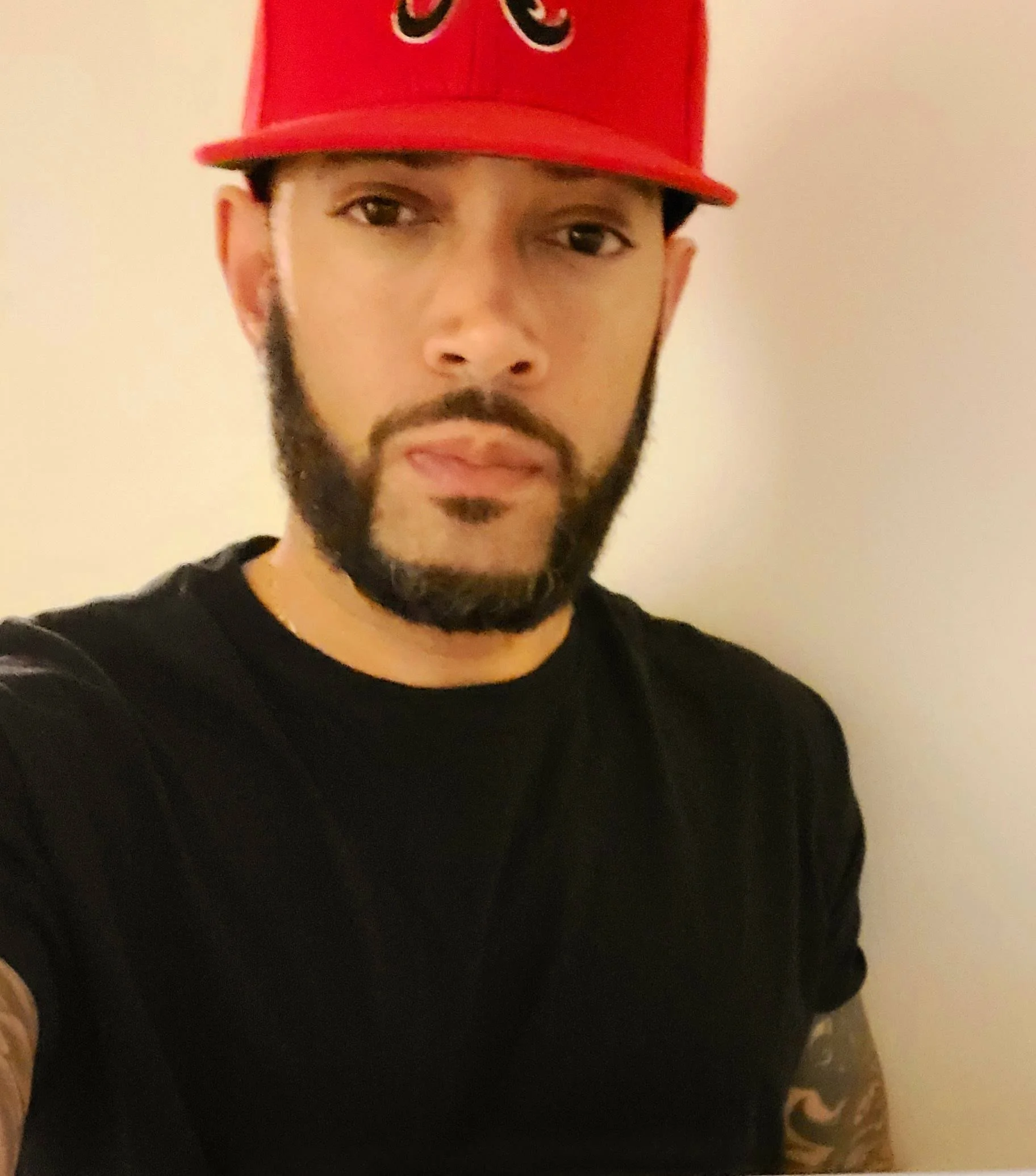 Person wearing a red cap and black shirt with tattoos on arm