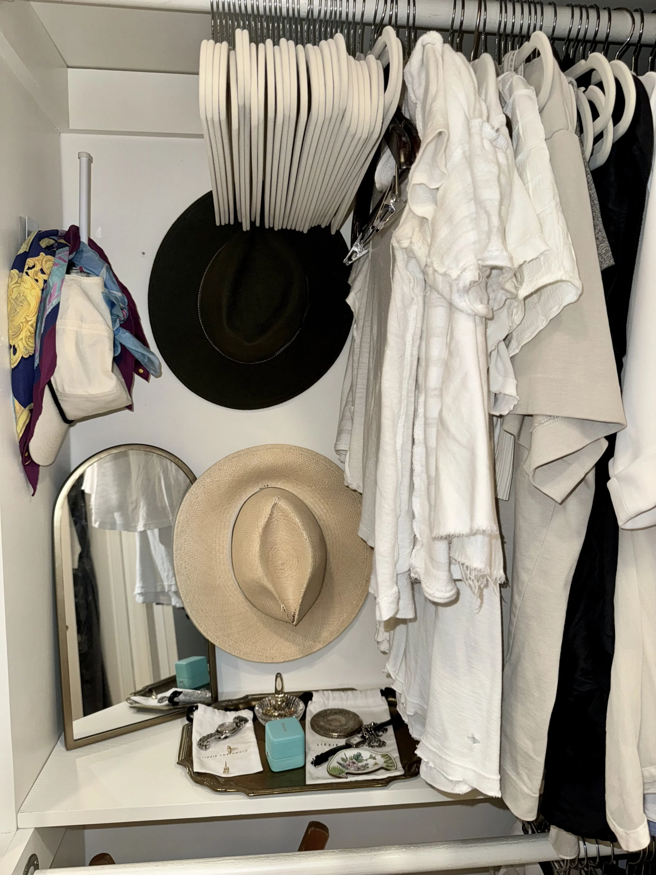 Closet in Kansas City with clothes and accessories hanging and placed in a closet, including hats, scarves, a mirror, and jewelry.